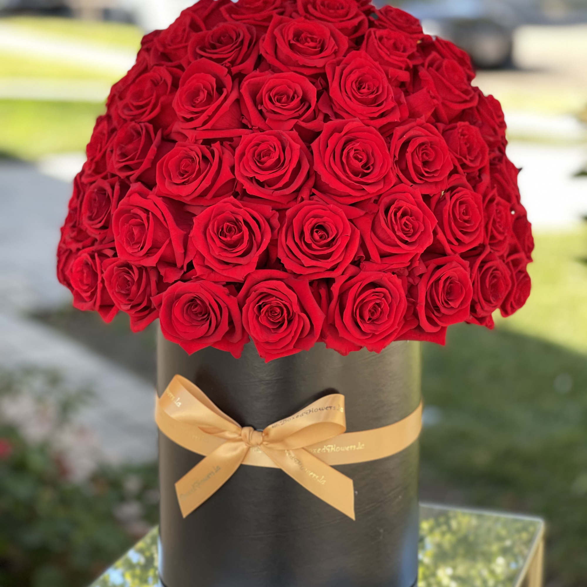 Large bouquet of red roses in a black hat box with a gold ribbon