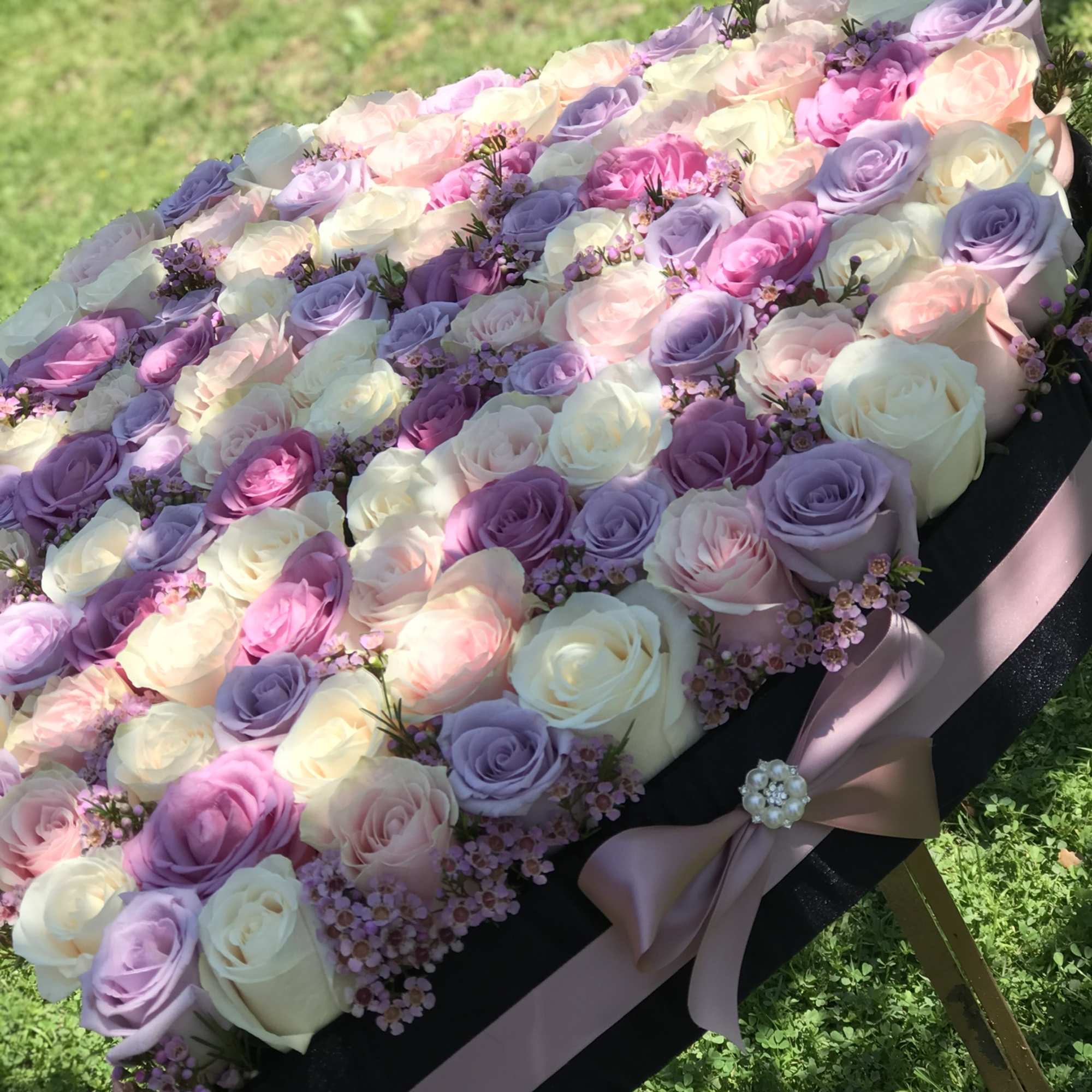 Pastel roses arranged on a black casket with a pink ribbon.