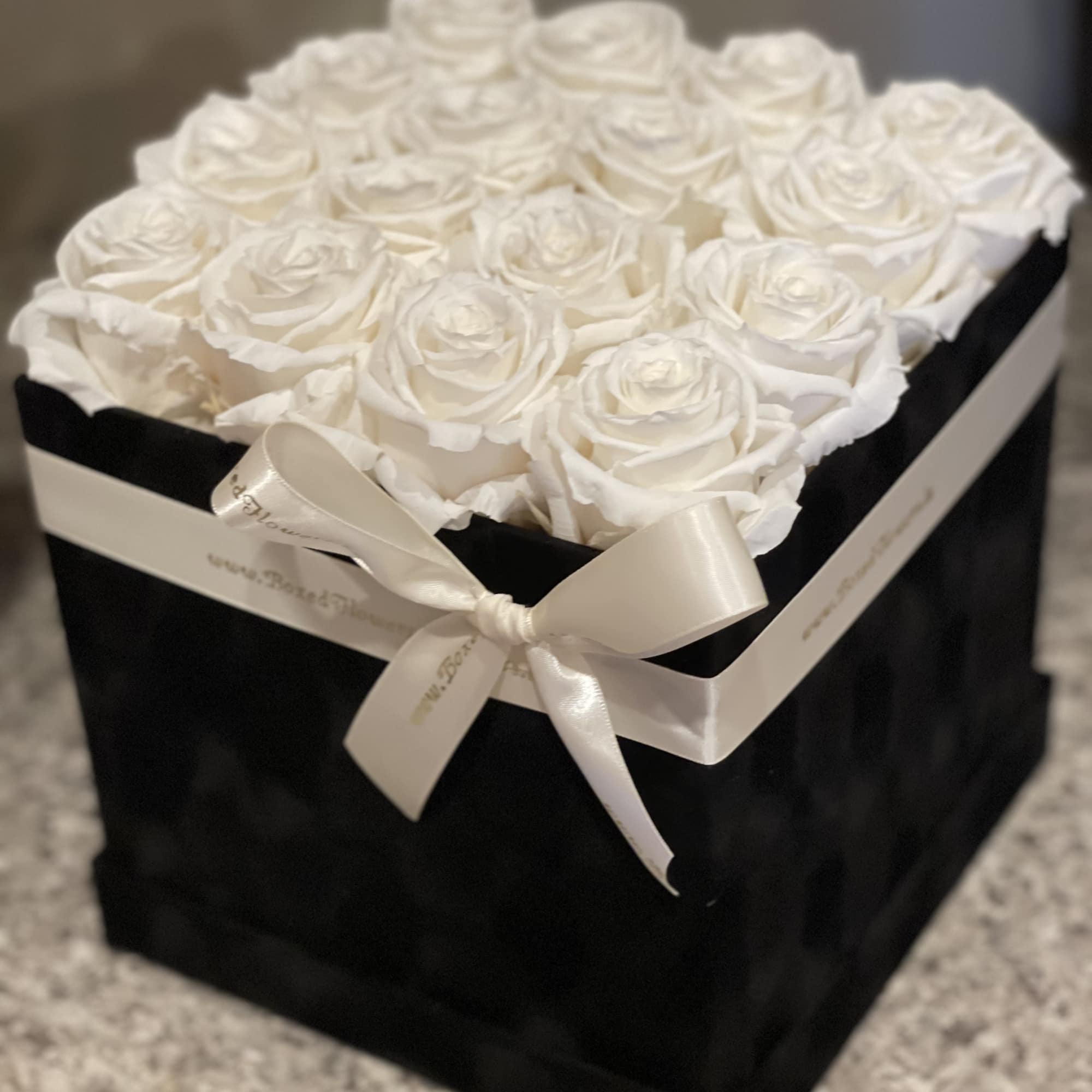 White roses arranged in a black square box with a satin ribbon bow