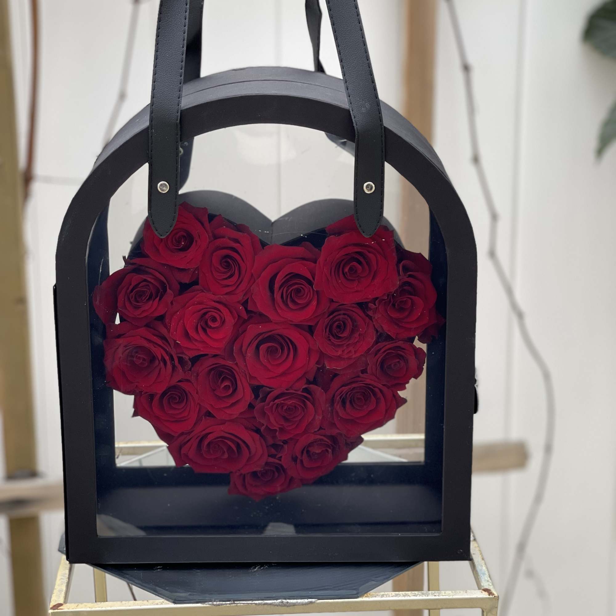 Heart-shaped box filled with red roses and black handles