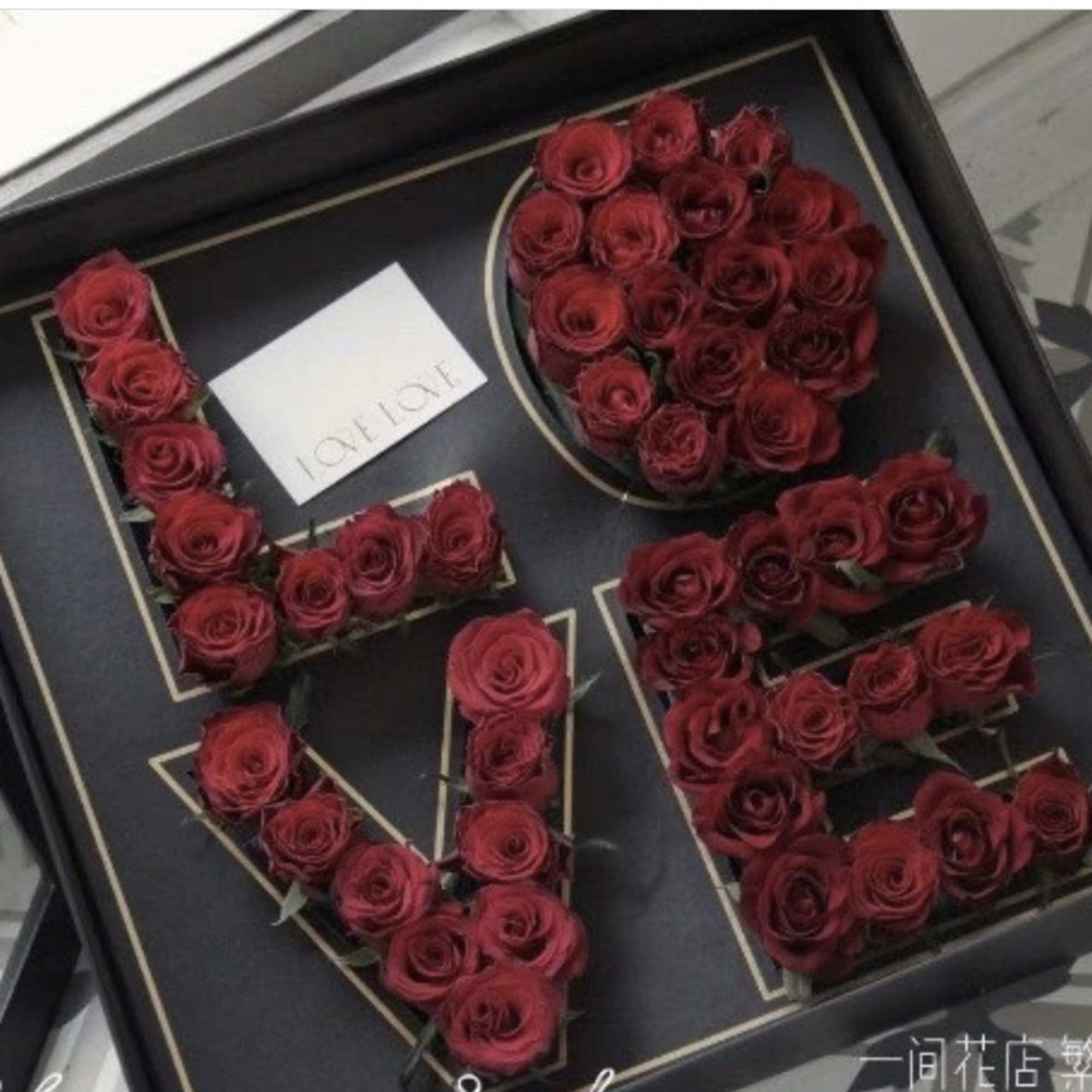 Red roses arranged in a black gift box to spell "LOVE"