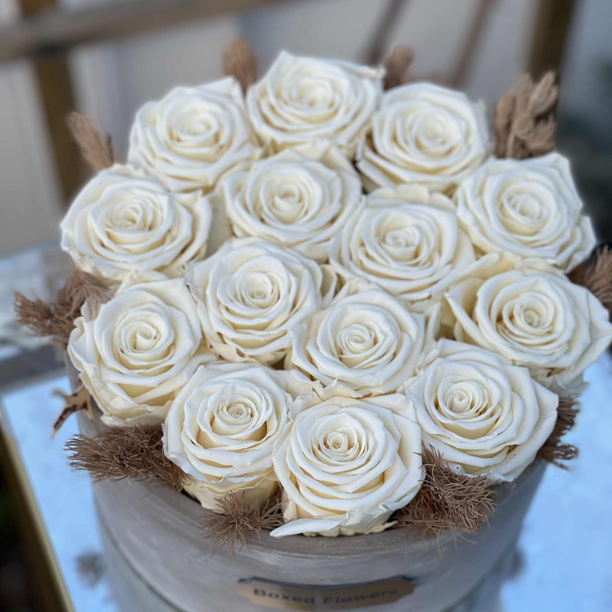 Round box of white roses with brown dried accents
