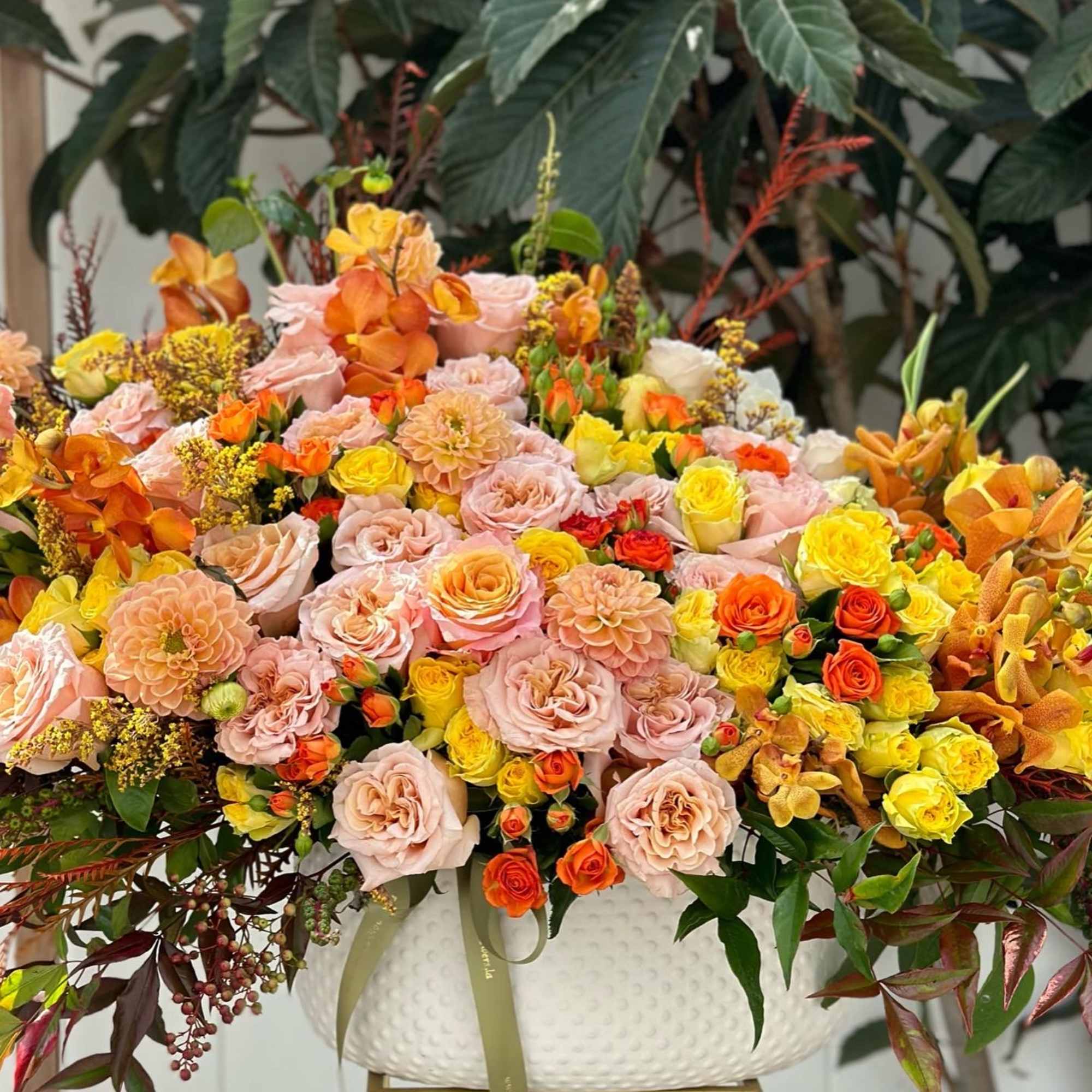 Large arrangement of pink, yellow, and orange roses in a white vase