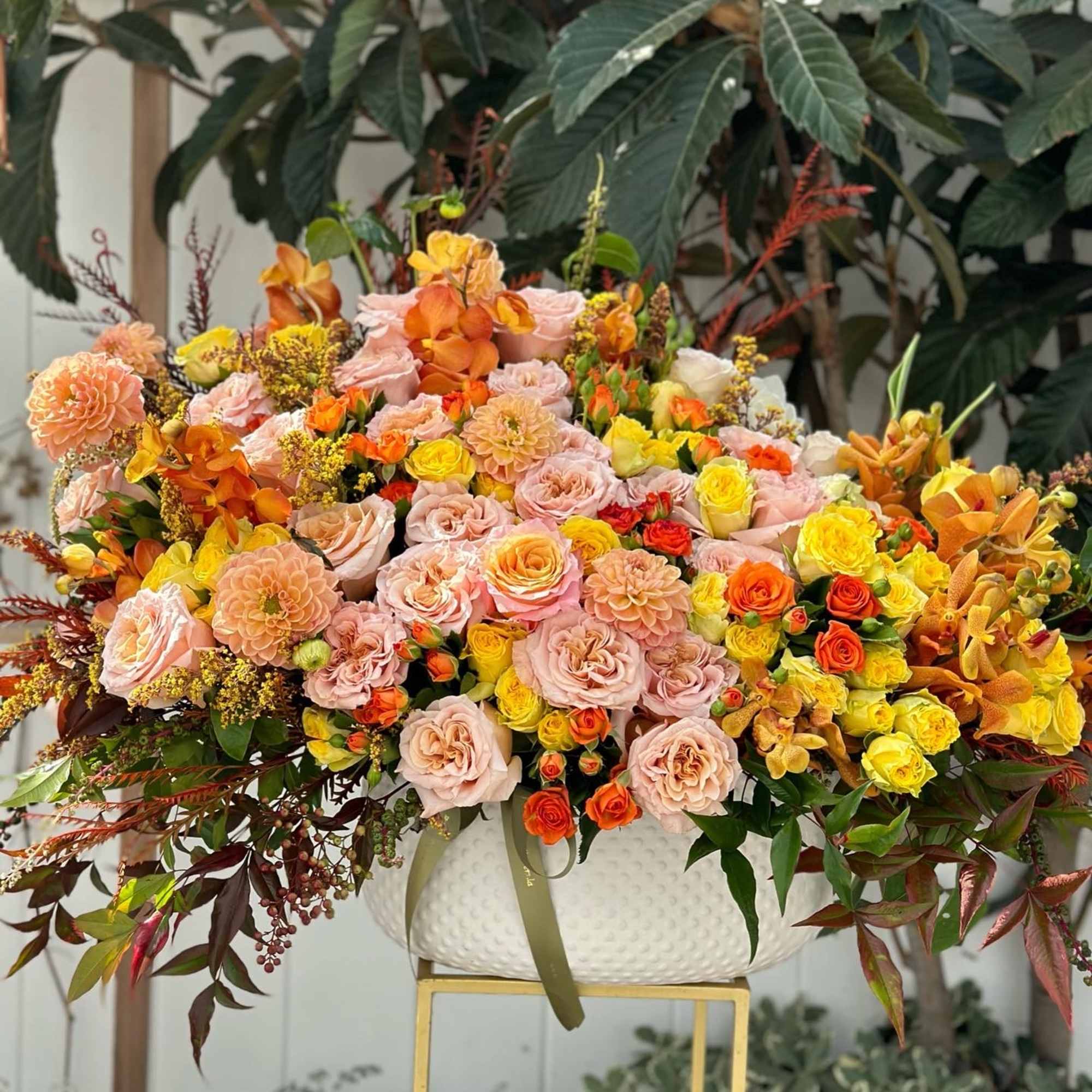 Large mixed bouquet of peach, pink, yellow, and orange flowers in a white vase