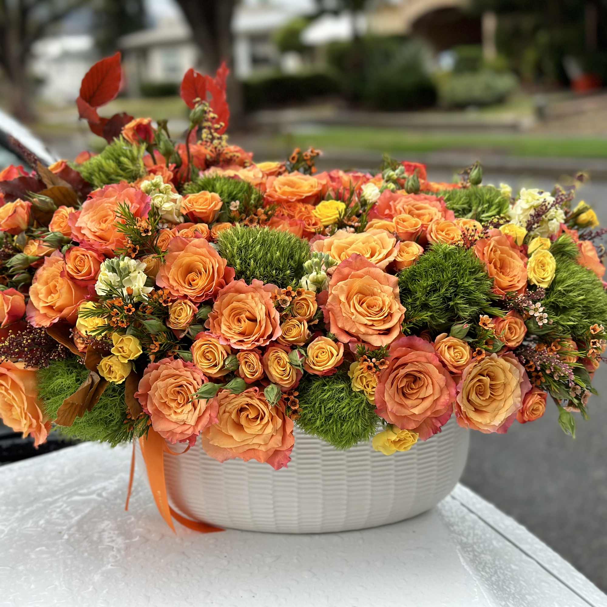 Orange rose arrangement in a white basket with green accents