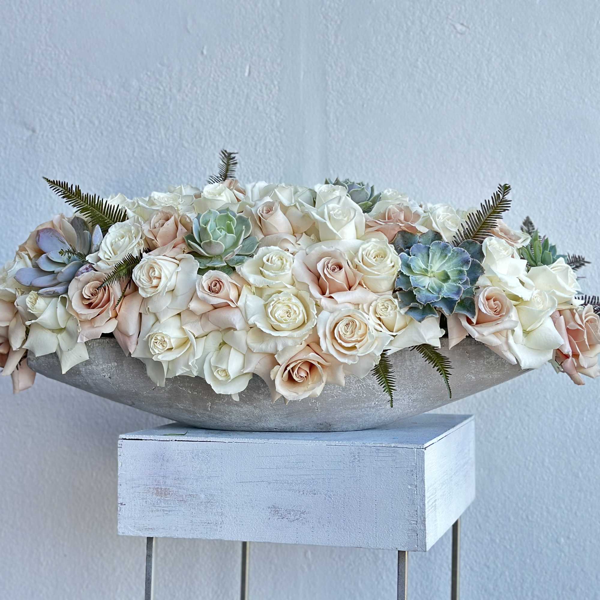 Low floral arrangement of blush and white roses with succulents in a shallow bowl