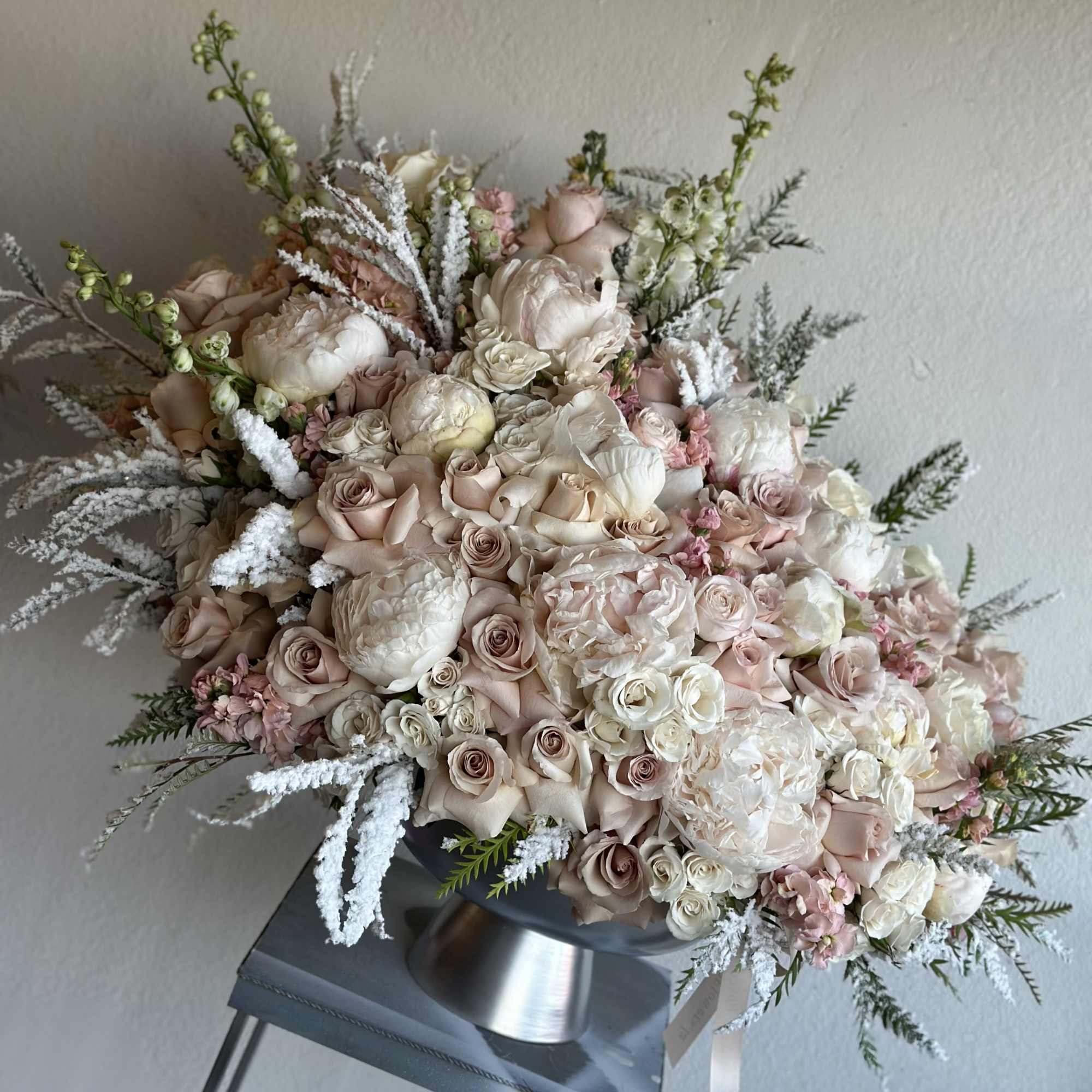 Silver vase filled with white and nuderoses, white peonies, and winter greenery.