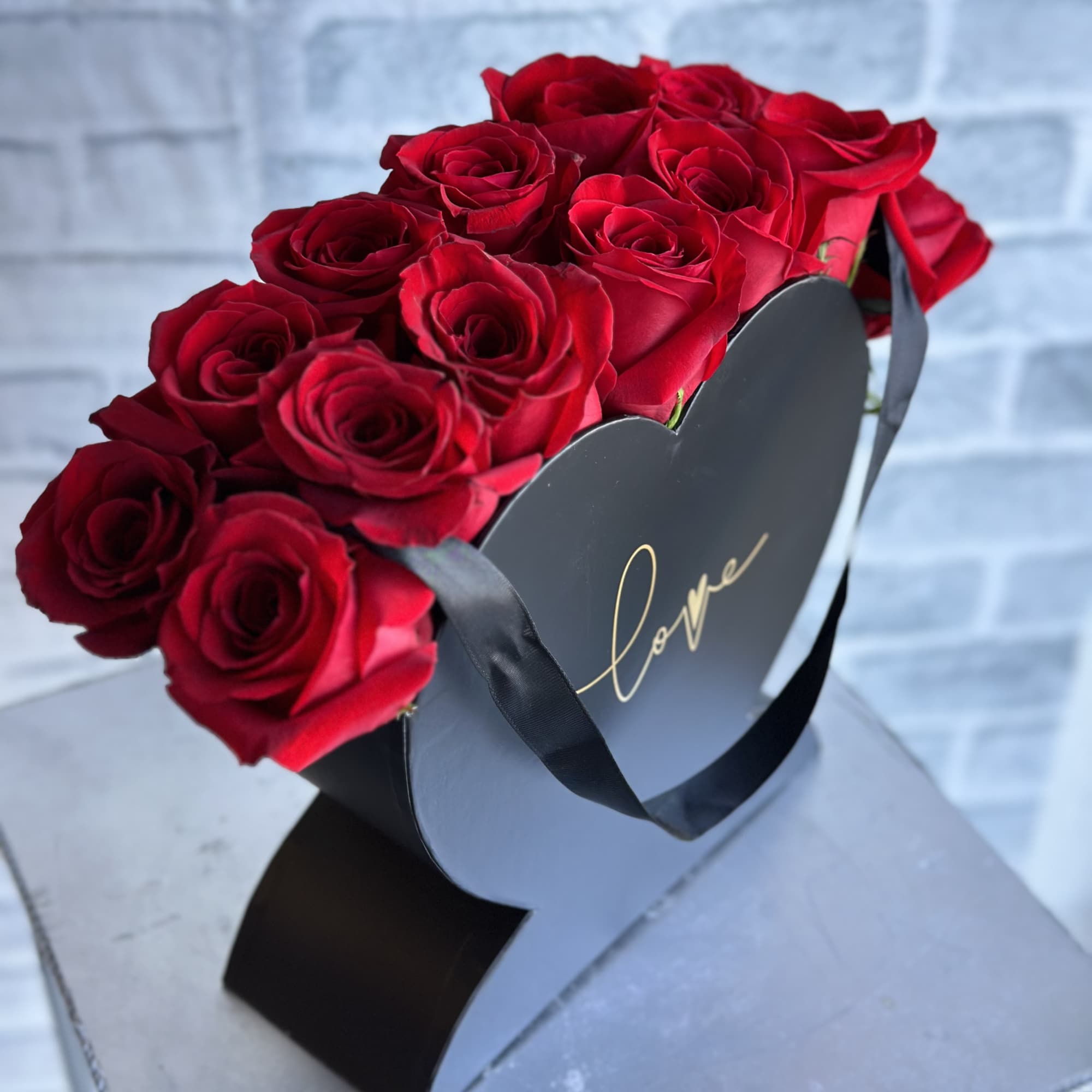Red roses arranged in a black heart-shaped box with a ribbon
