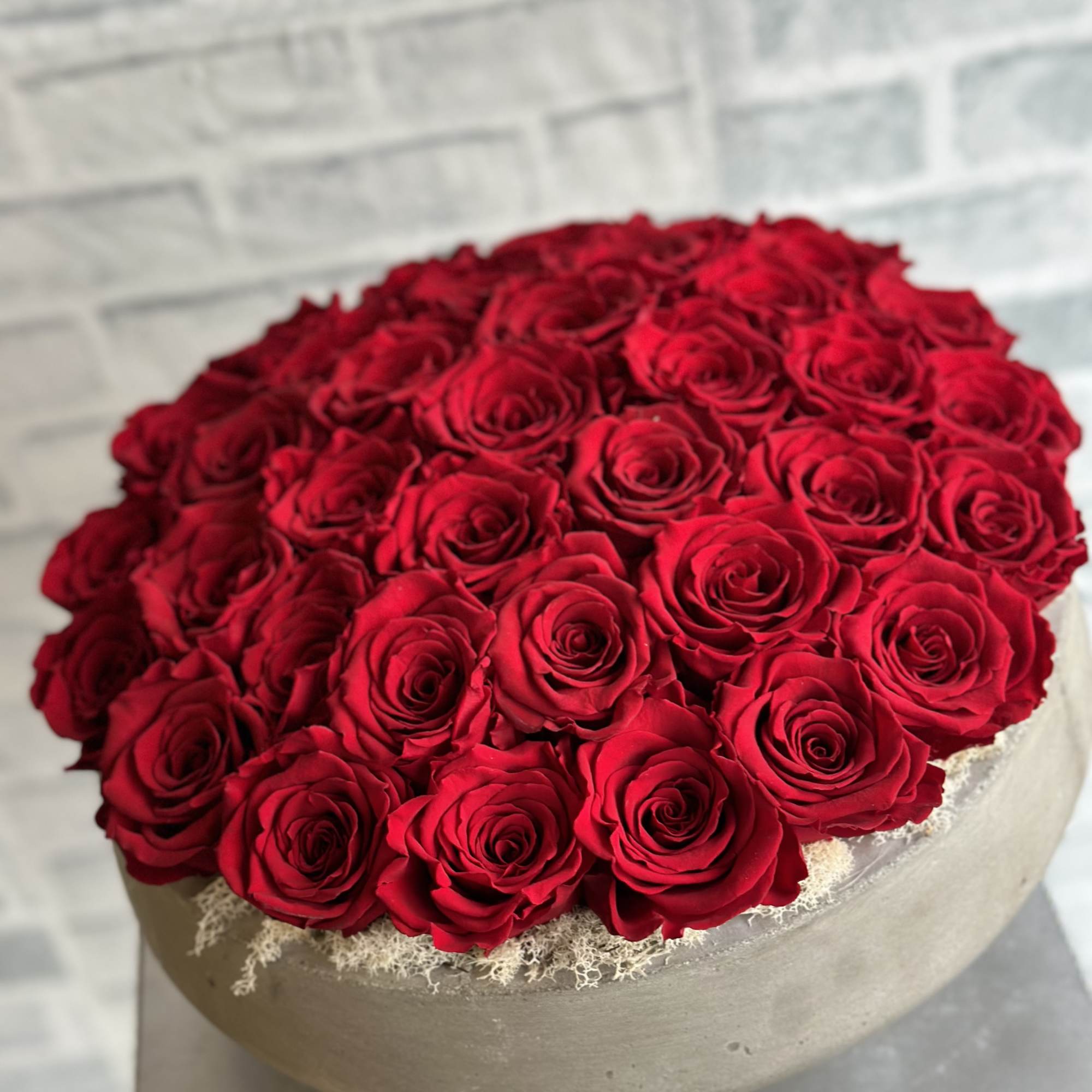 Round arrangement of red roses in a low beige container