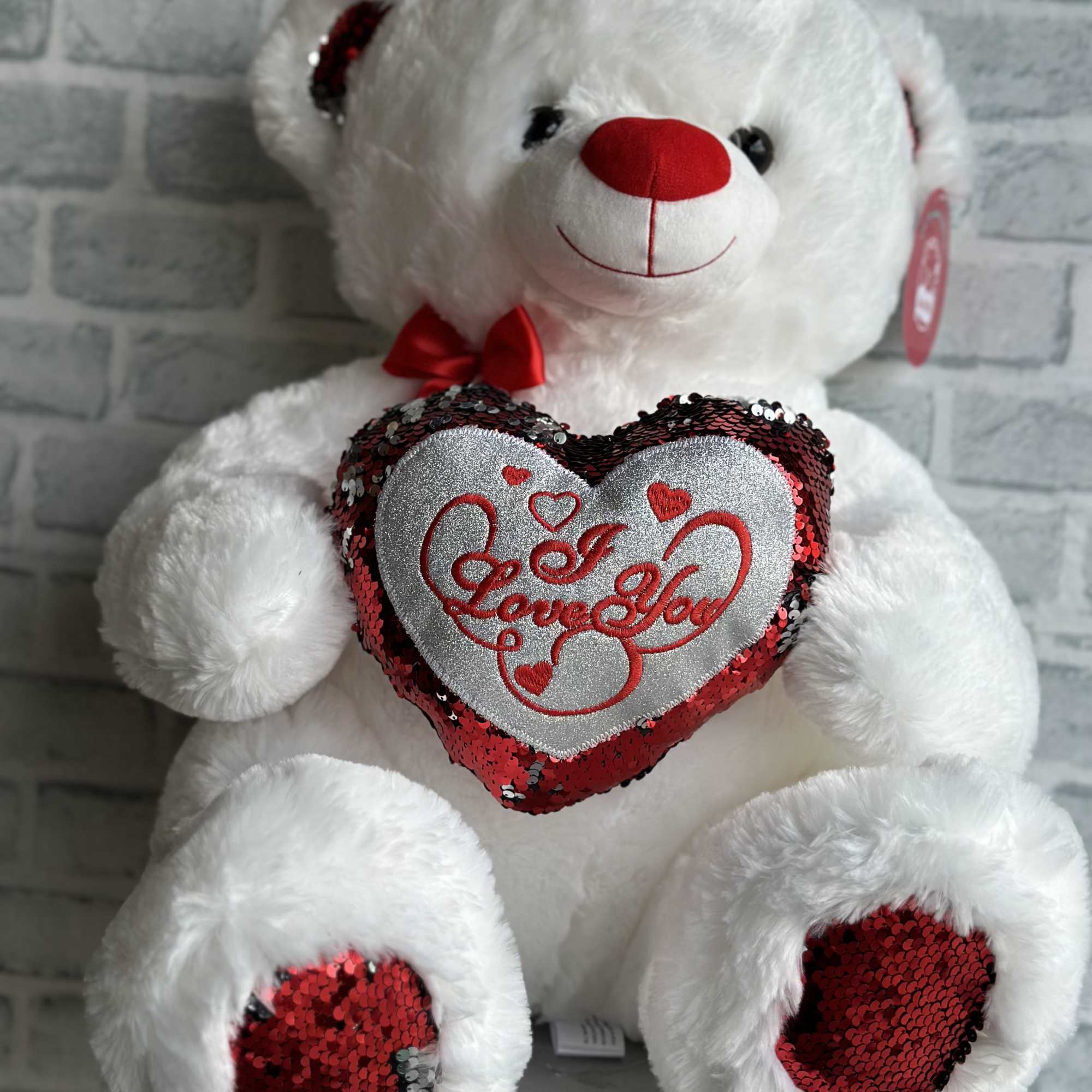 White teddy bear holding a sequined heart that says Love You