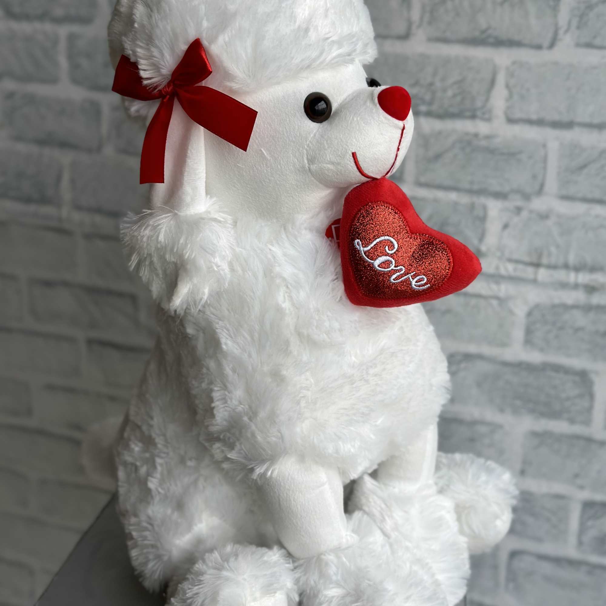 White plush teddy bear holding a red heart with the word Love