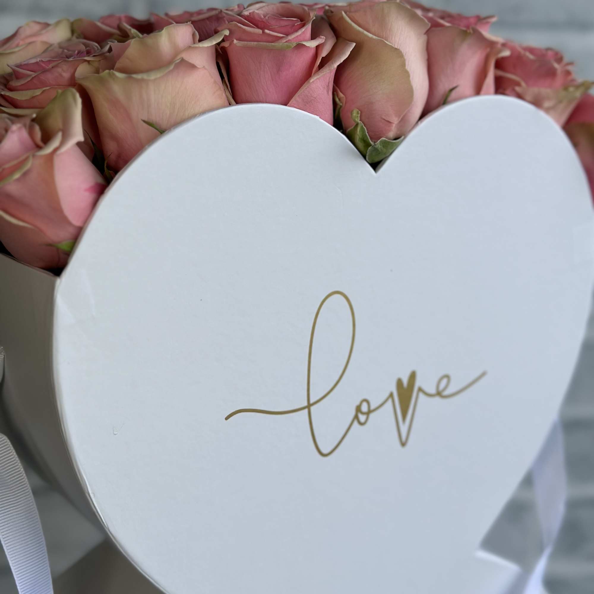 Pink roses in a white heart-shaped box with "love" on the front