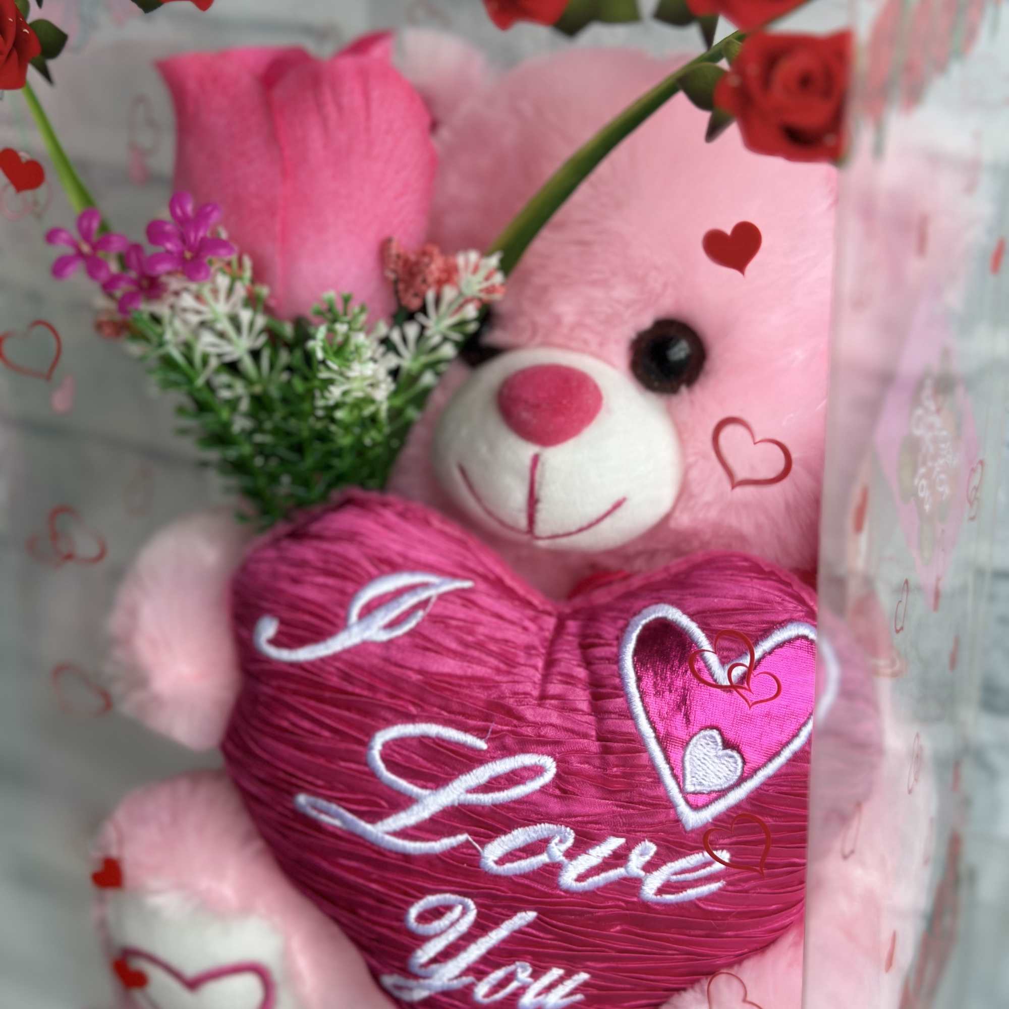 Pink teddy bear holding a heart with red roses around it