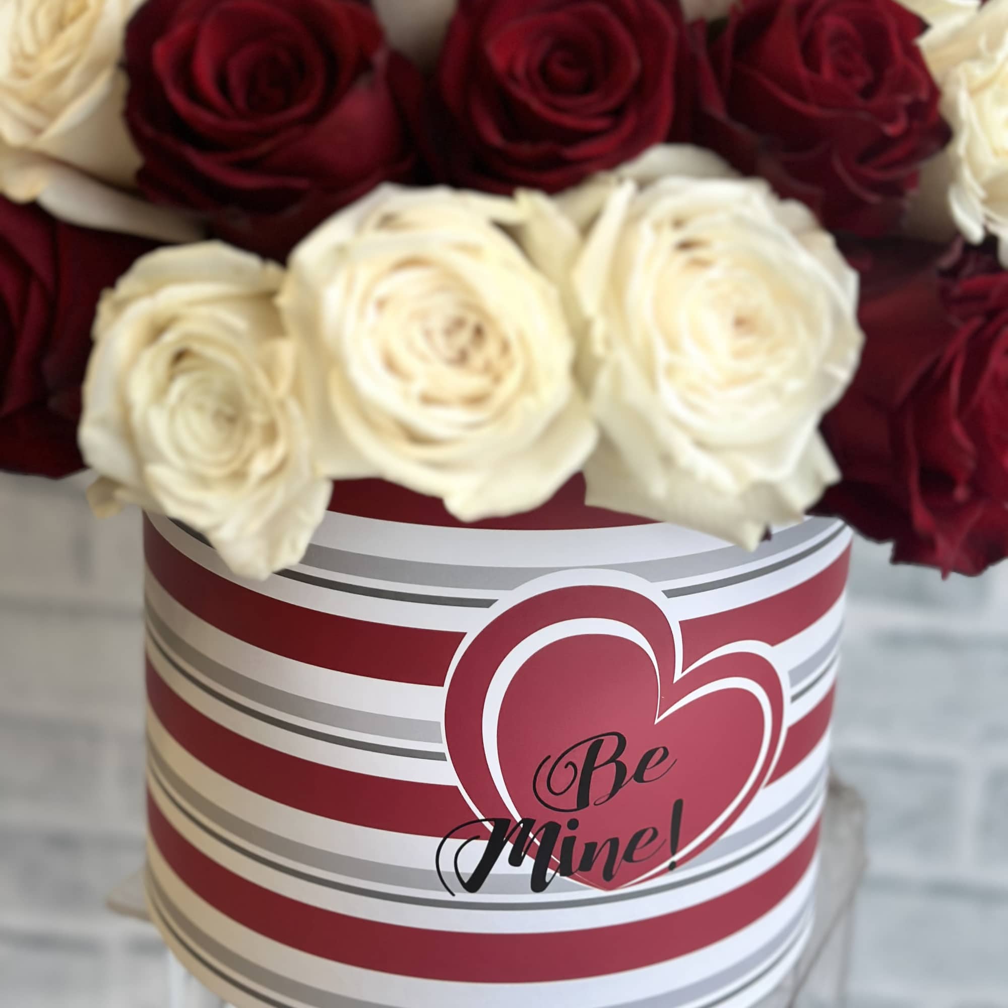 Red and white roses in a striped heart-themed box with "Be Mine" text