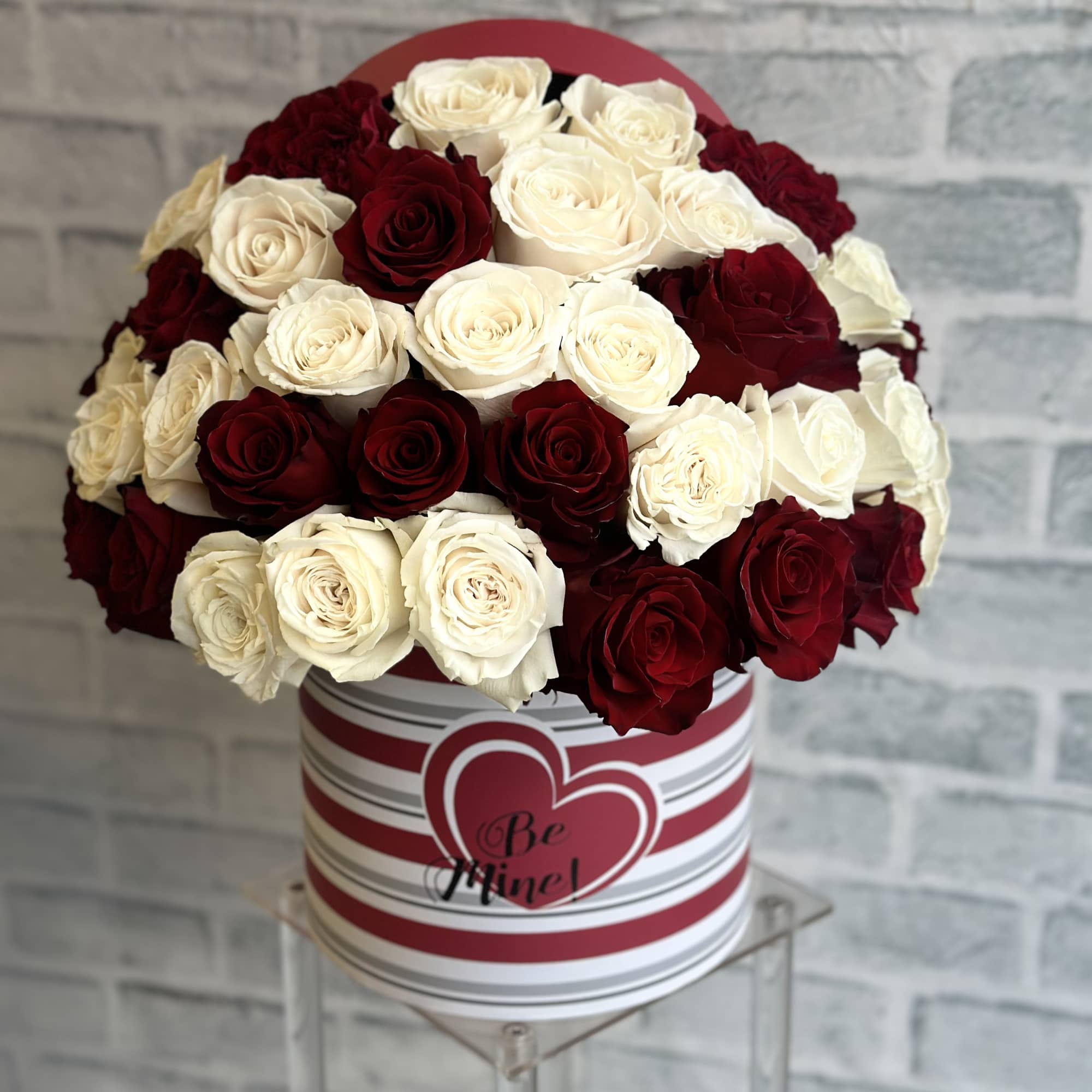 Red and white rose arrangement in a striped heart box