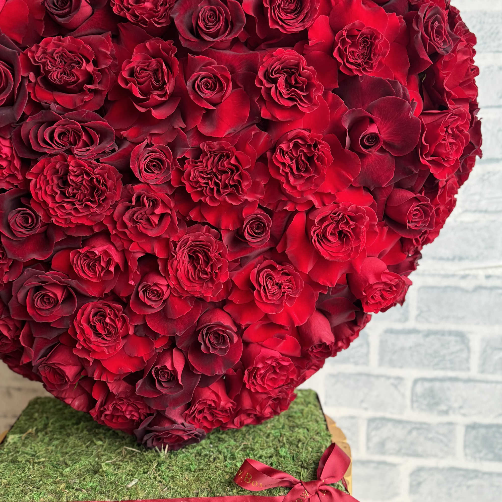 Heart-shaped arrangement of red roses on a wooden base with a ribbon