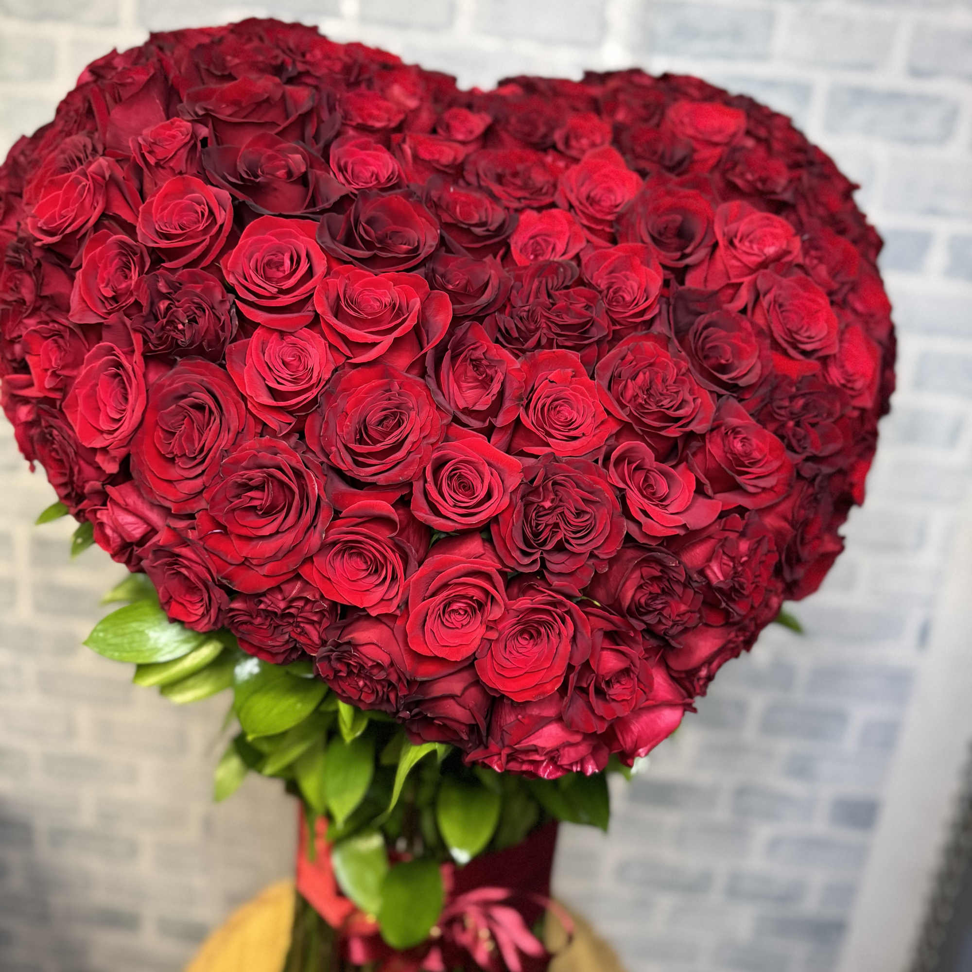 Heart-shaped bouquet of red roses with green leaves and a ribbon wrap
