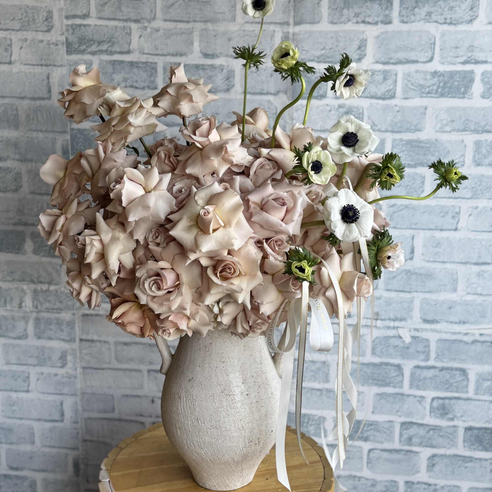 Blush roses in a white vase with white anemones and ribbon accents