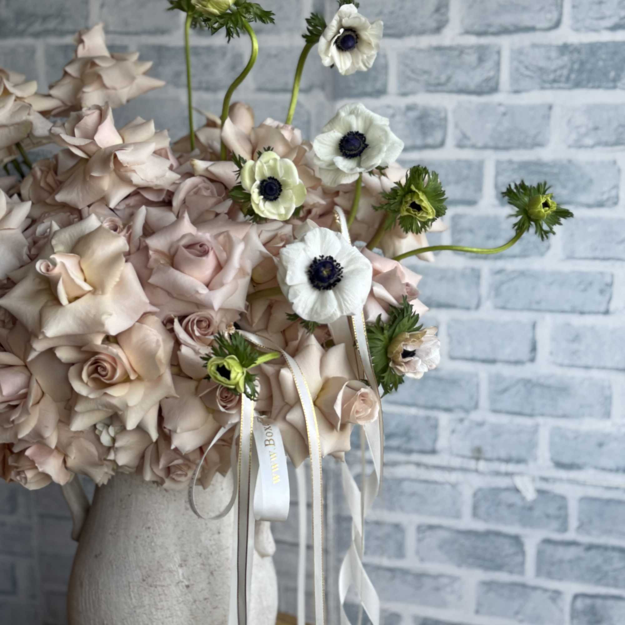 Blush roses with white anemones in a tall ceramic vase