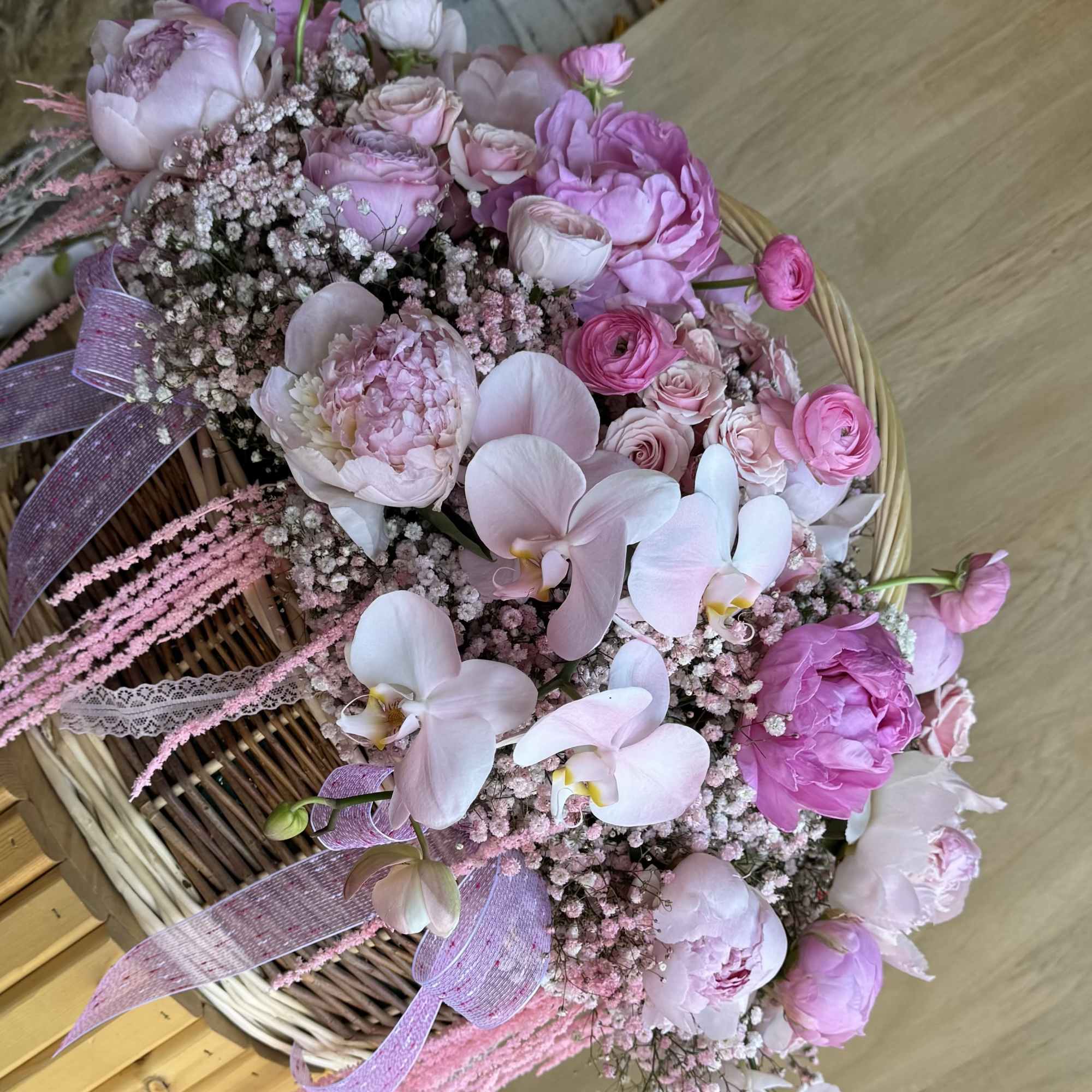 Pink floral arrangement in a wicker basket with ribbon accents