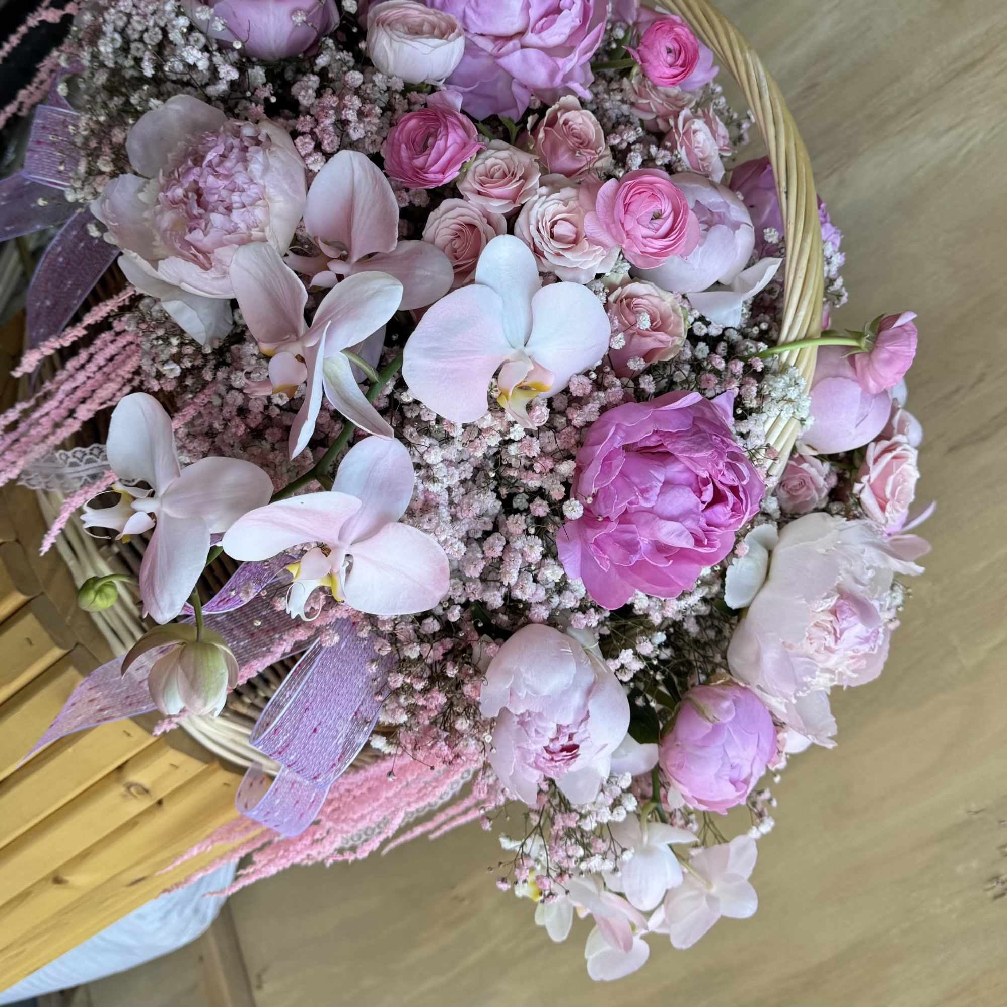 Pink and white bouquet with orchids, roses, and peonies in a wicker basket