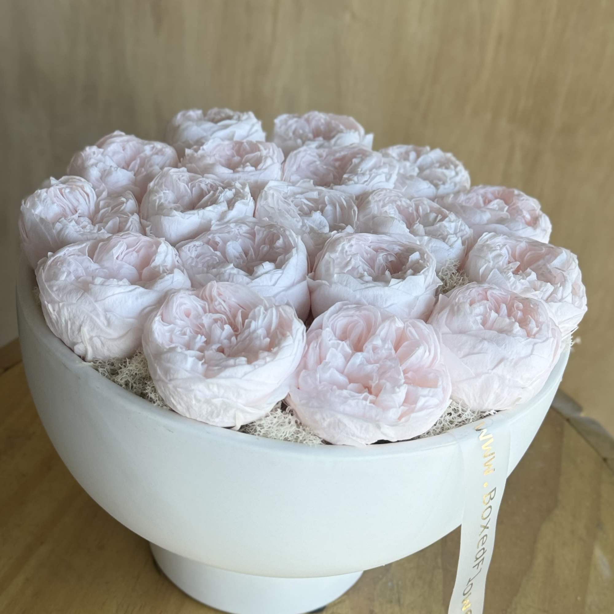 Round box of pale pink peonies with a ribbon tag