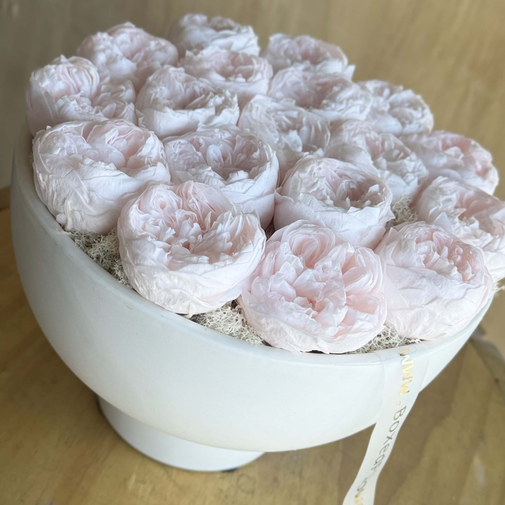 Round box of pale pink peonies on a wooden surface