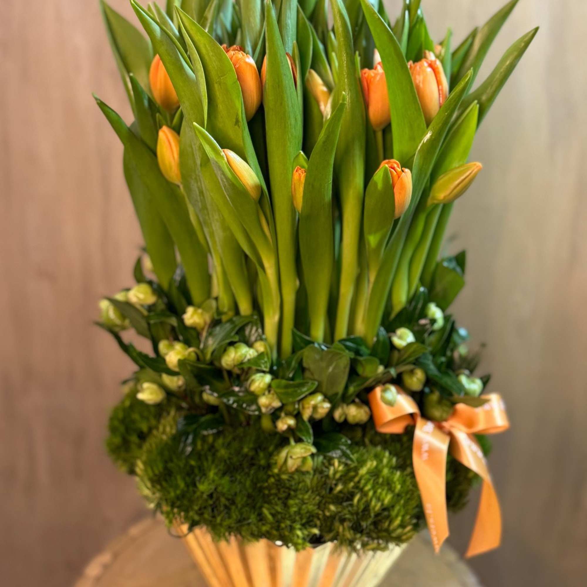 Orange tulips arranged in a gold vase with a ribbon