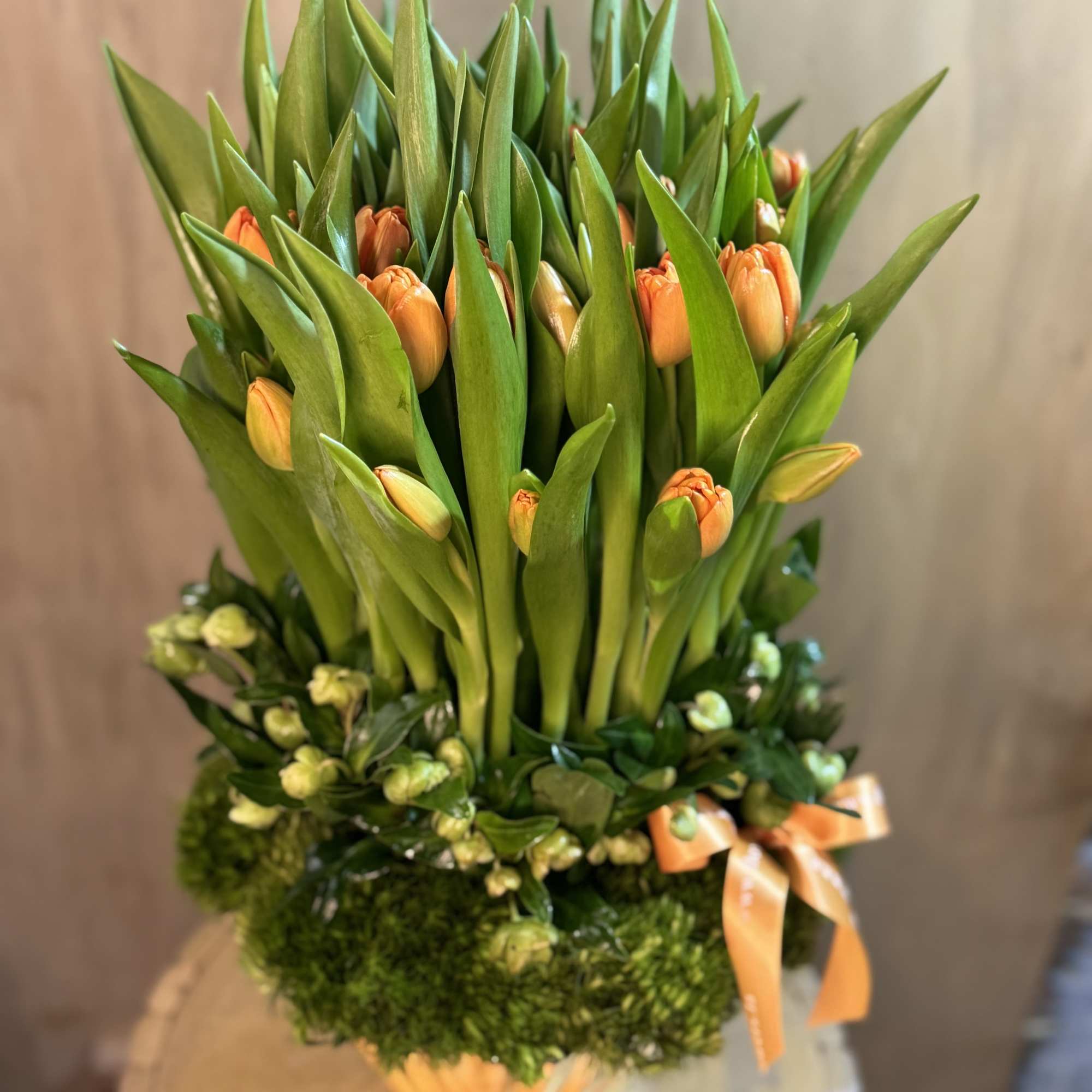 Orange tulips arranged in a tall green bouquet with a ribbon