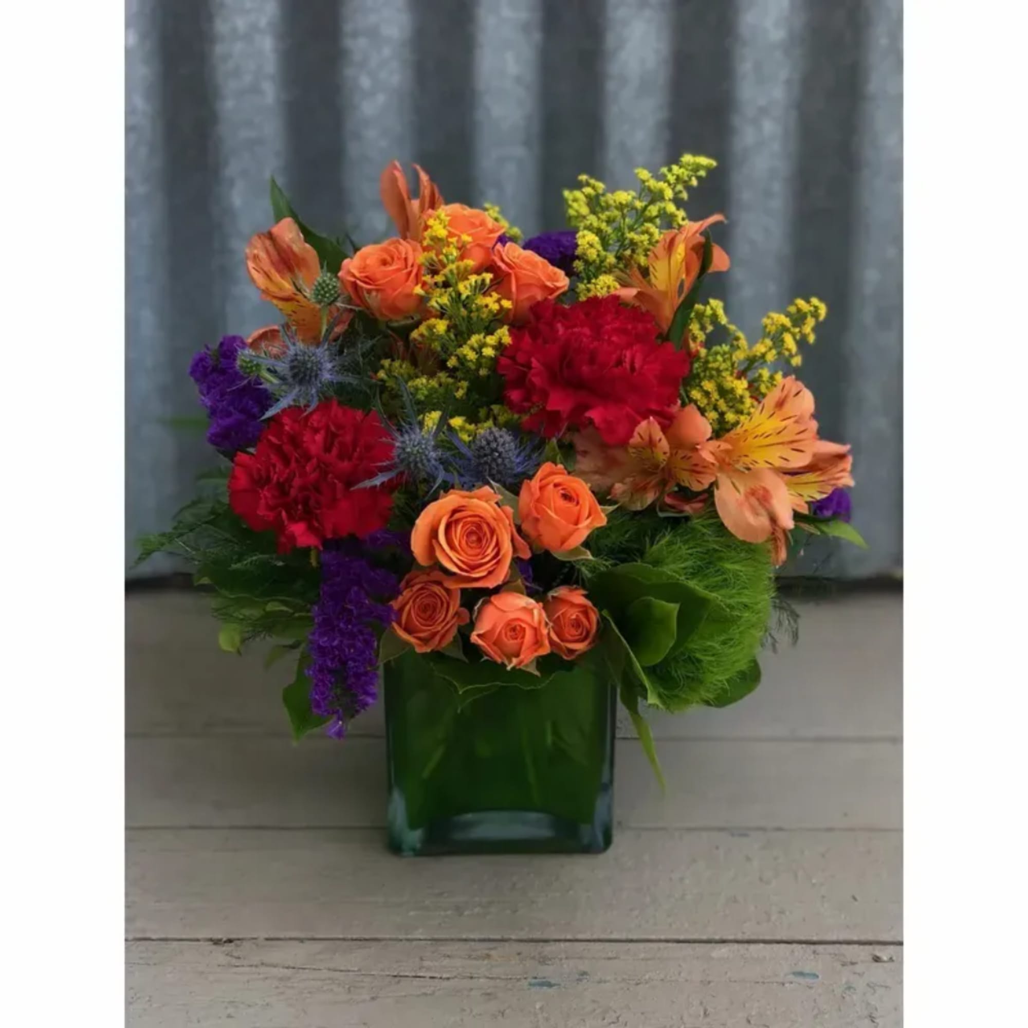 Colorful bouquet of orange and red flowers in a green glass vase