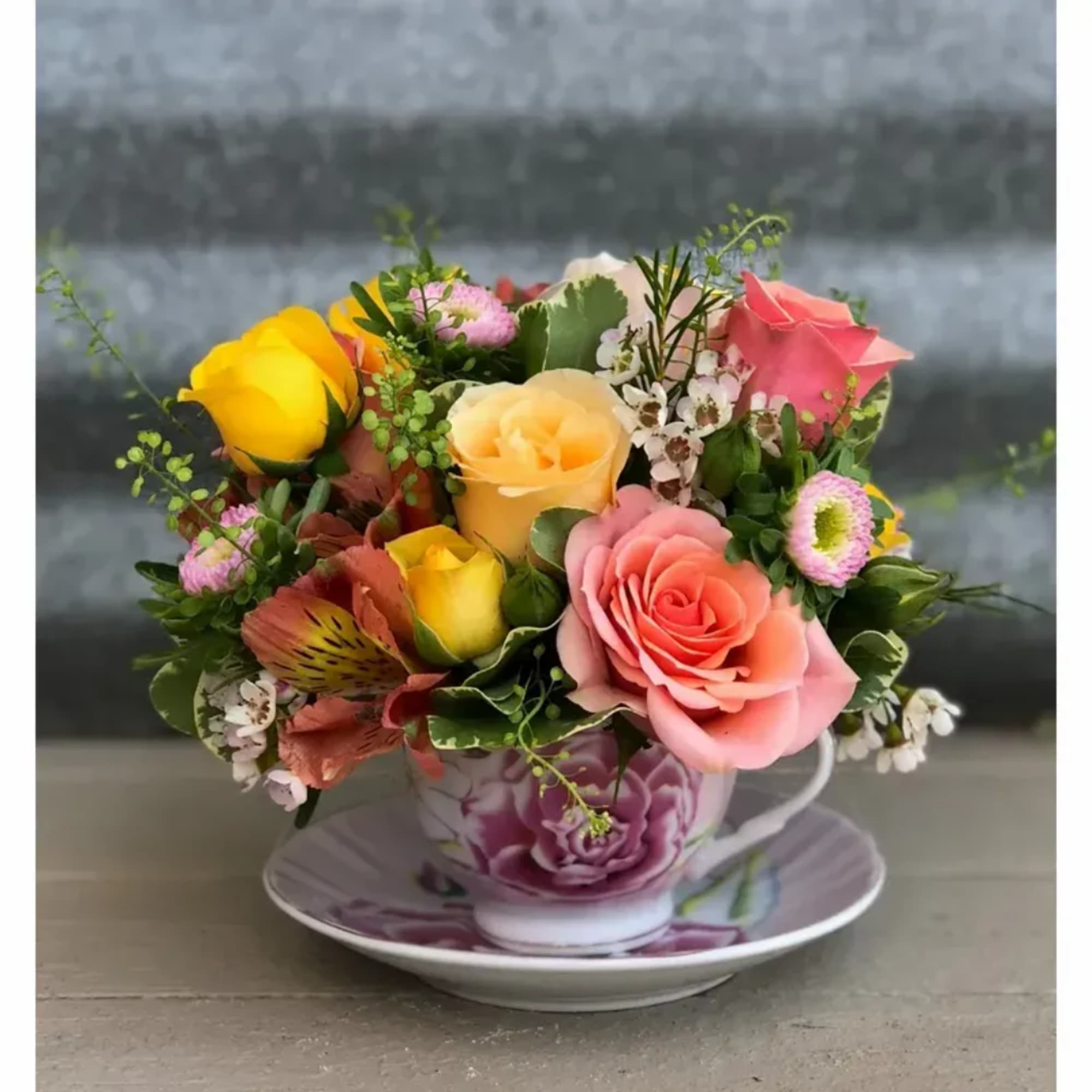 Mixed roses arranged in a floral teacup on a saucer