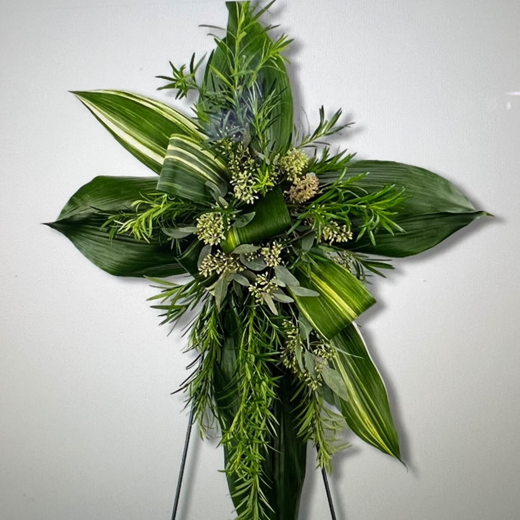 Green floral cross with layered leaves and small white blooms