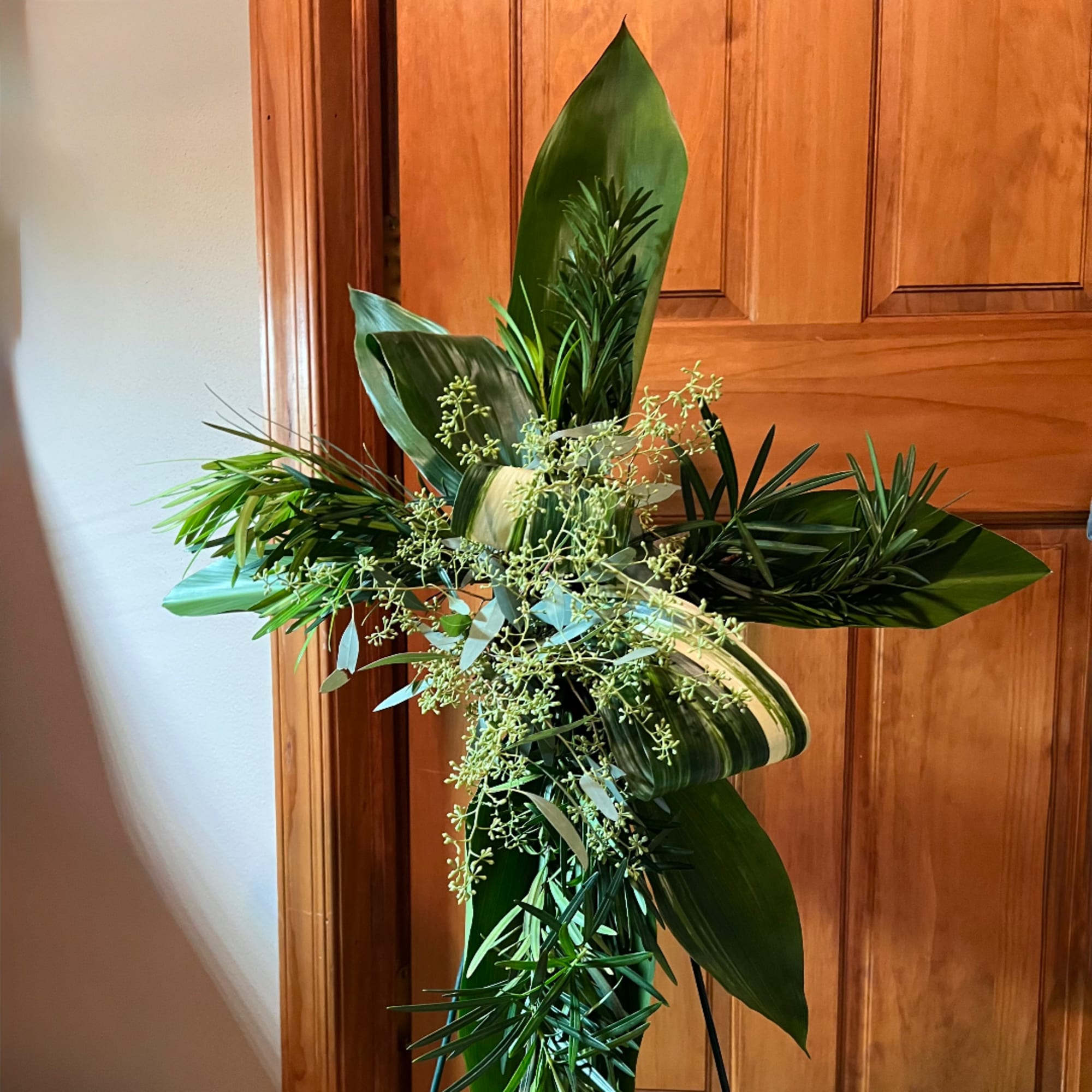 Tall green floral cross with layered leaves and delicate filler