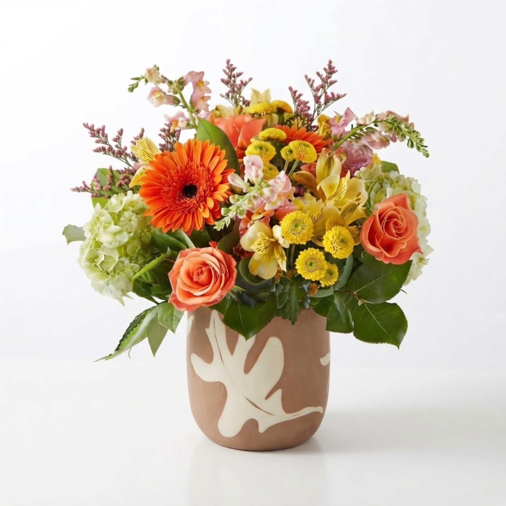 Mixed bouquet of orange, yellow, and pink flowers in a patterned vase