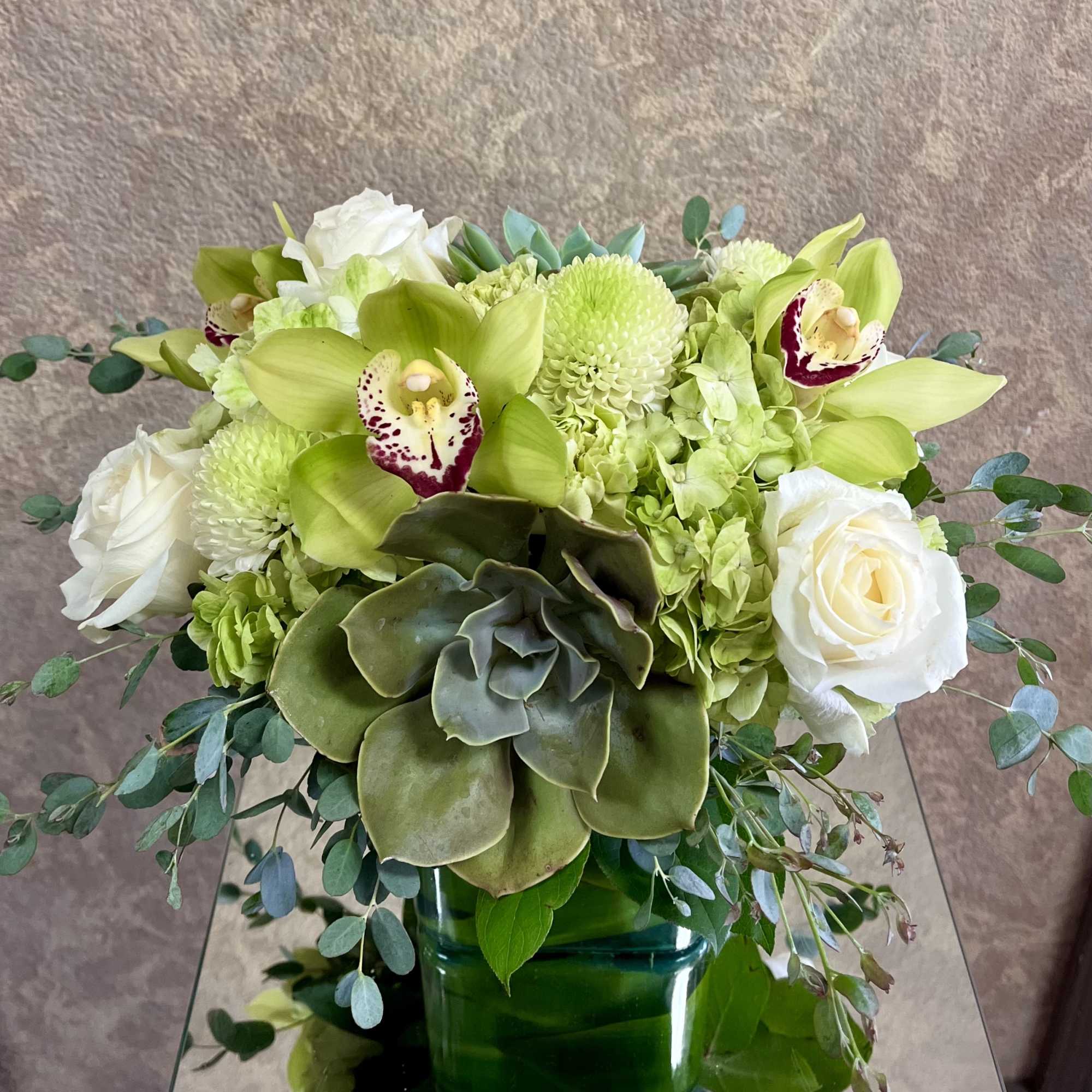 Green and white floral arrangement in a green vase with orchids and roses