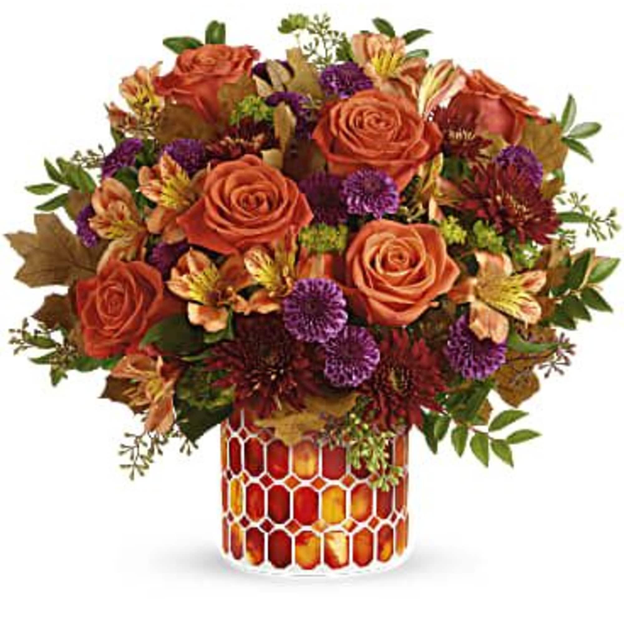Orange roses and purple flowers arranged in a patterned glass vase