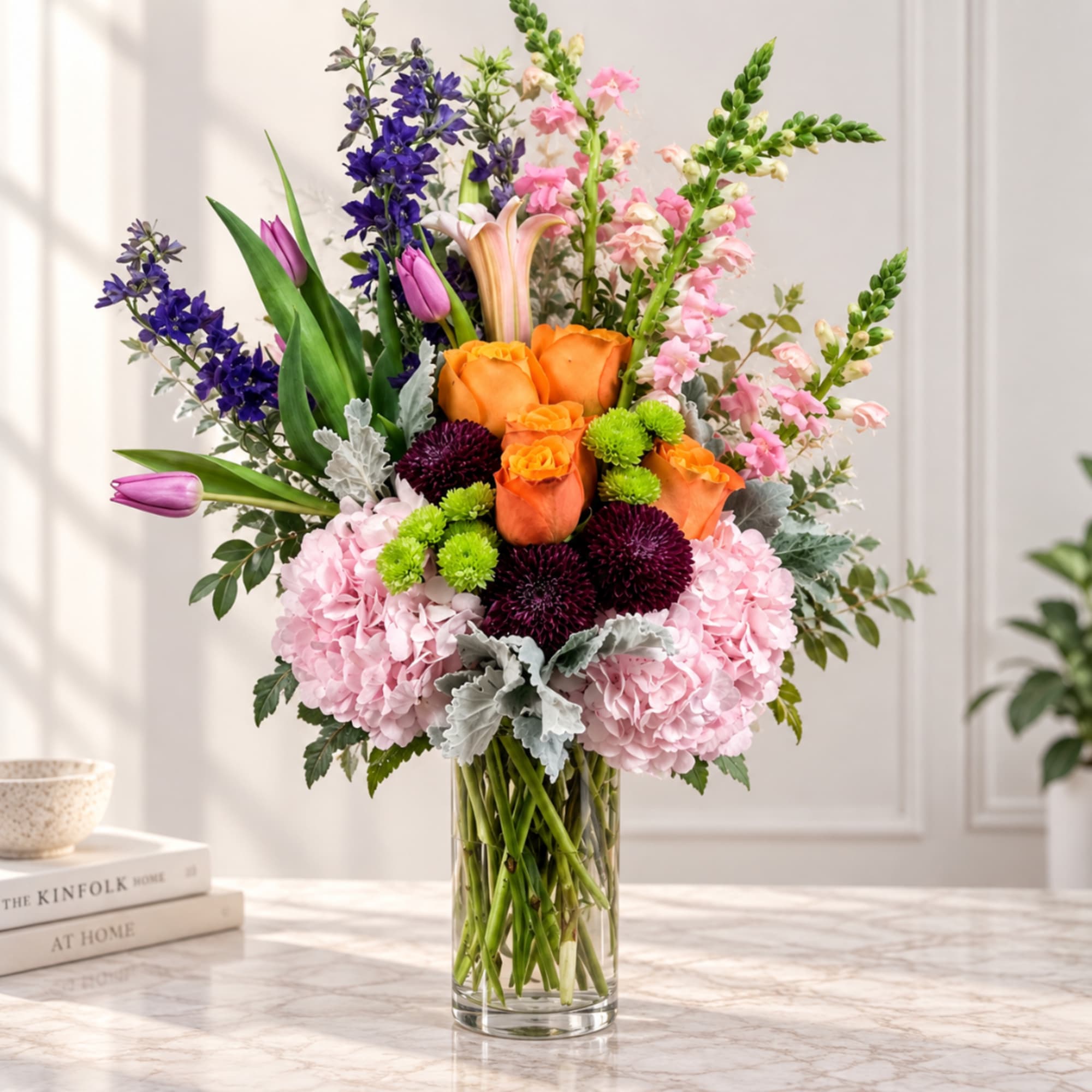 Mixed bouquet of orange roses, pink hydrangeas, and purple flowers in a clear glass vase