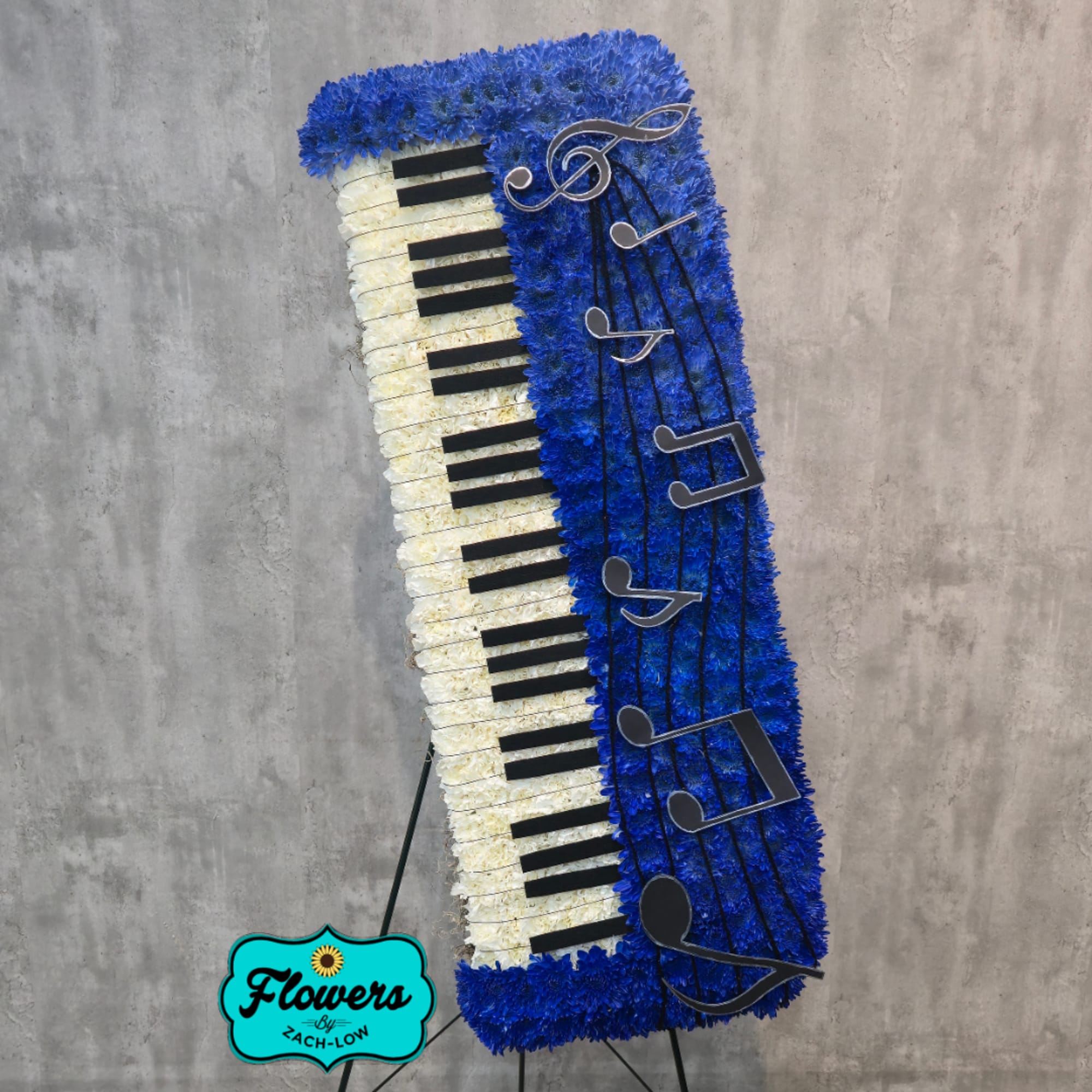 Tall floral tribute shaped like a piano keyboard with blue and white flowers