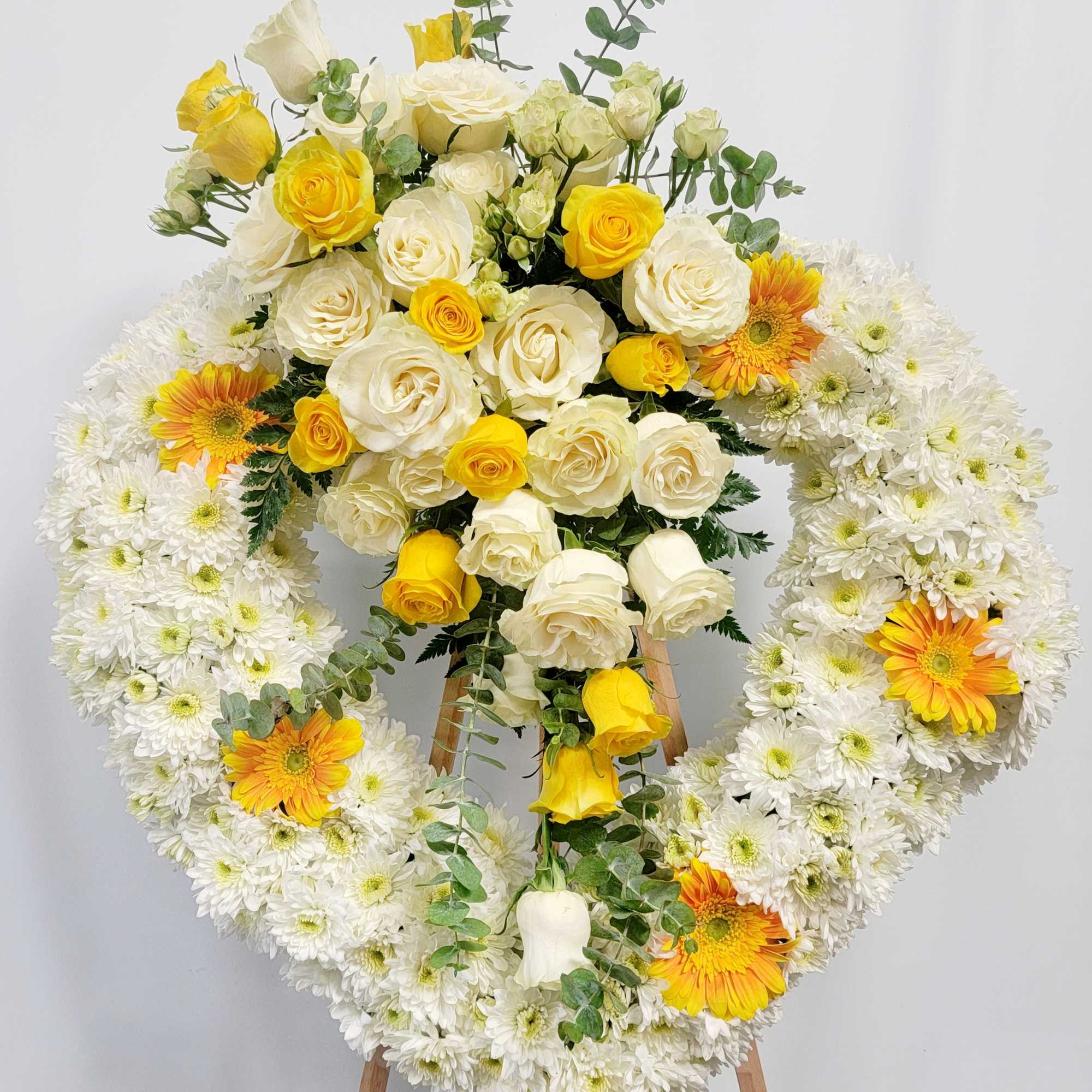 Heart-shaped floral wreath with white chrysanthemums, yellow roses, and orange gerberas