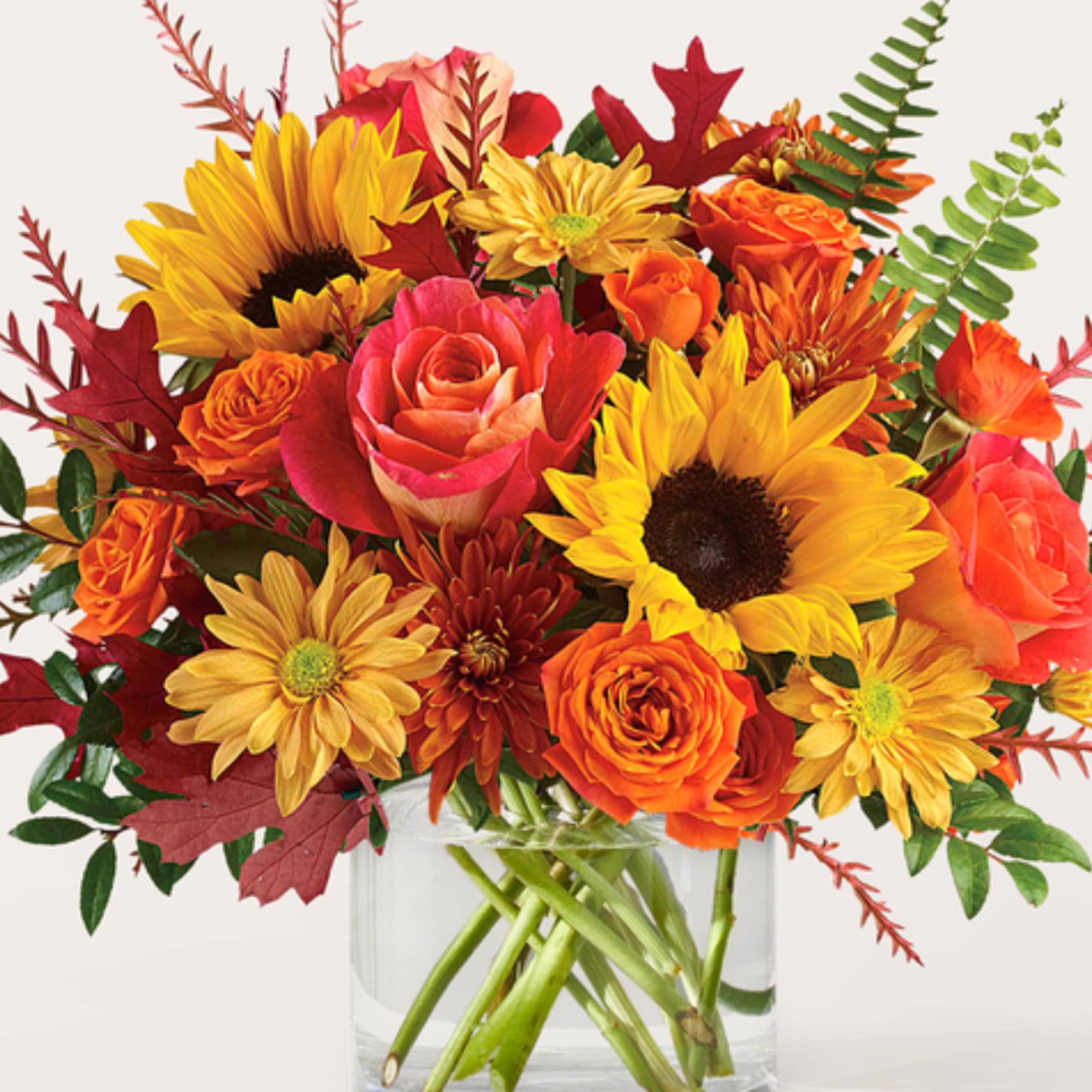 Mixed bouquet of sunflowers, roses, and mums in a clear glass vase