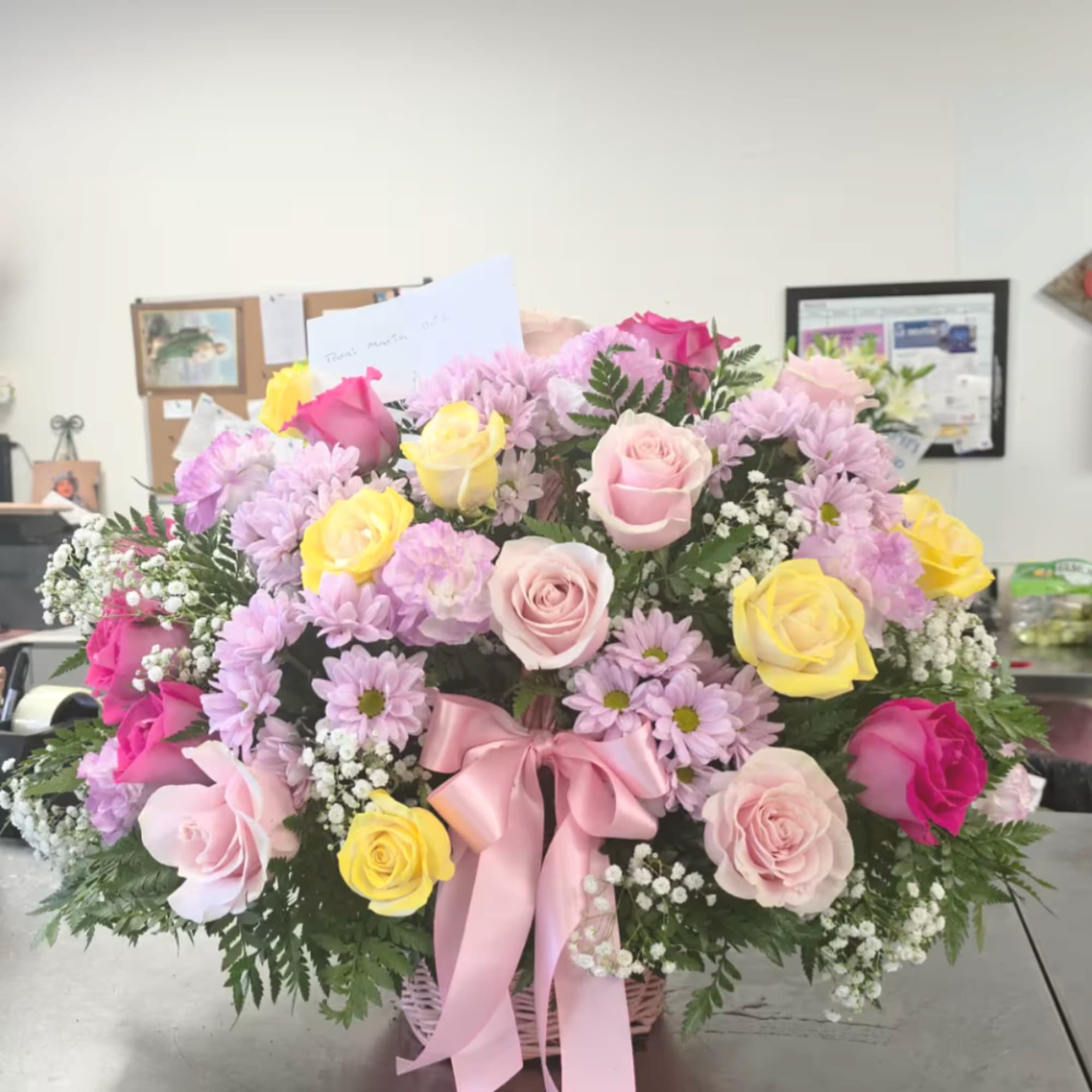 Basket arrangement of pink, yellow, and lavender flowers with a pink ribbon