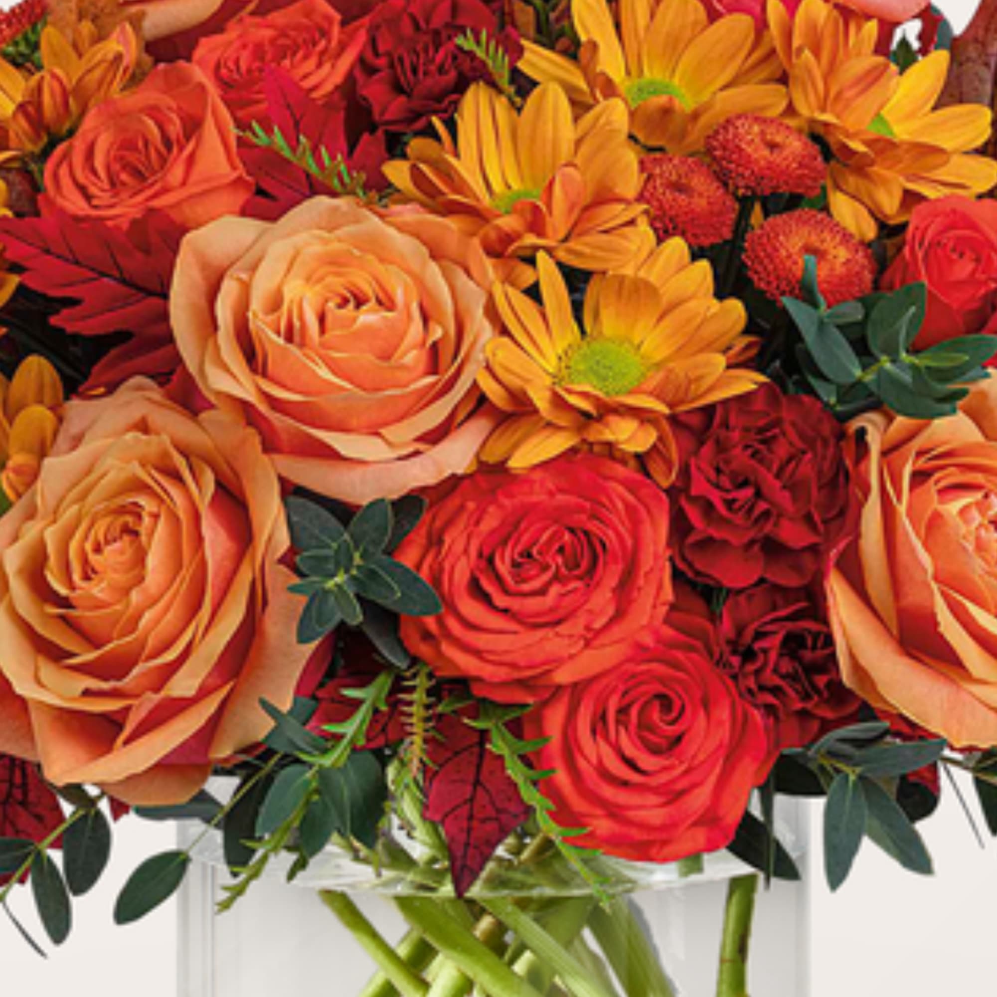 Orange and red roses with yellow daisies in a clear vase