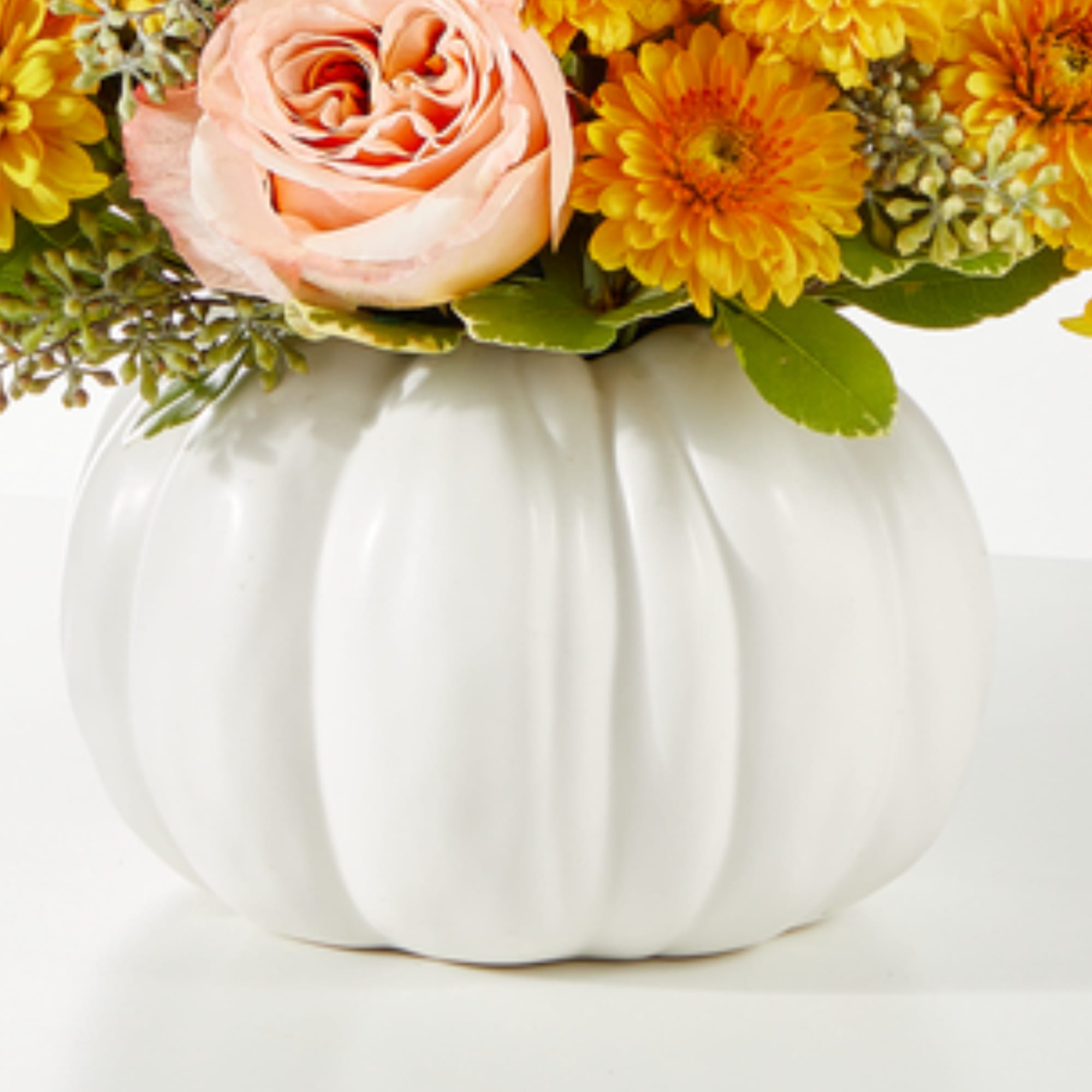 Pink rose and yellow flowers arranged in a white pumpkin vase