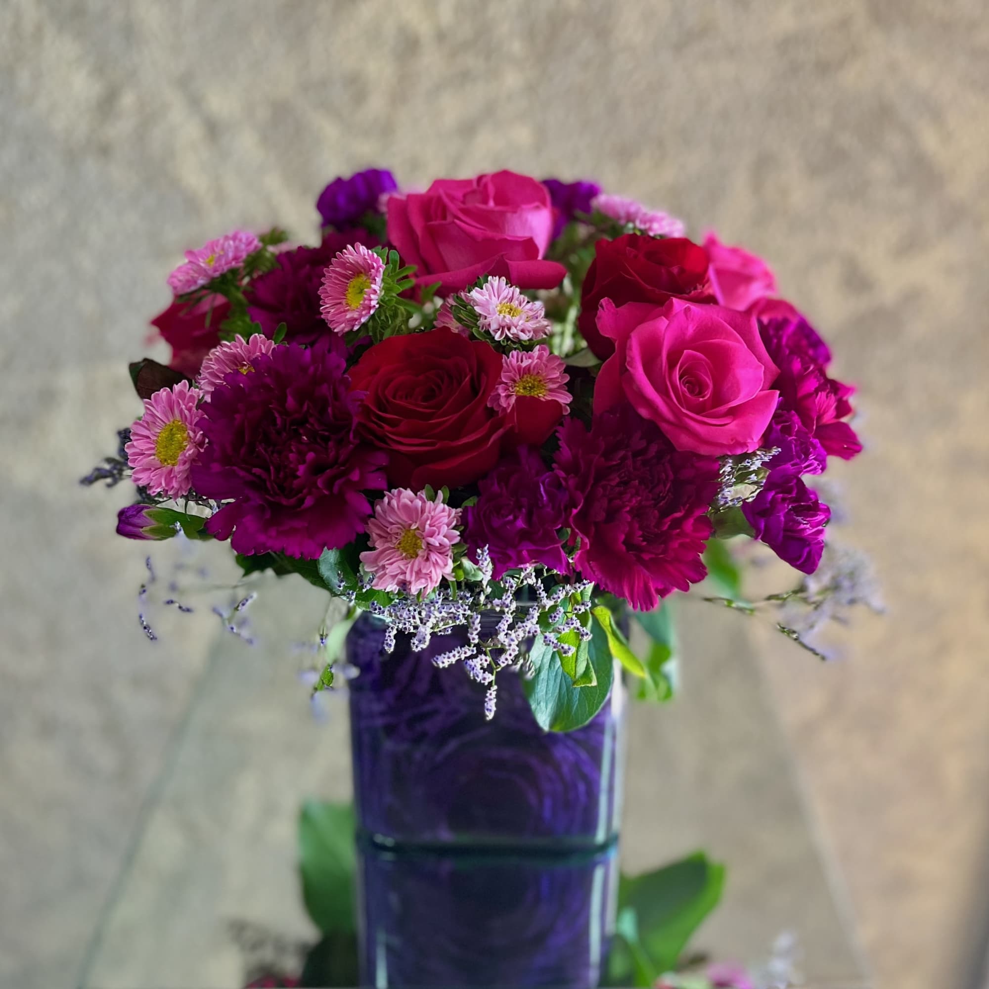 Pink and red roses with small purple flowers in a purple vase