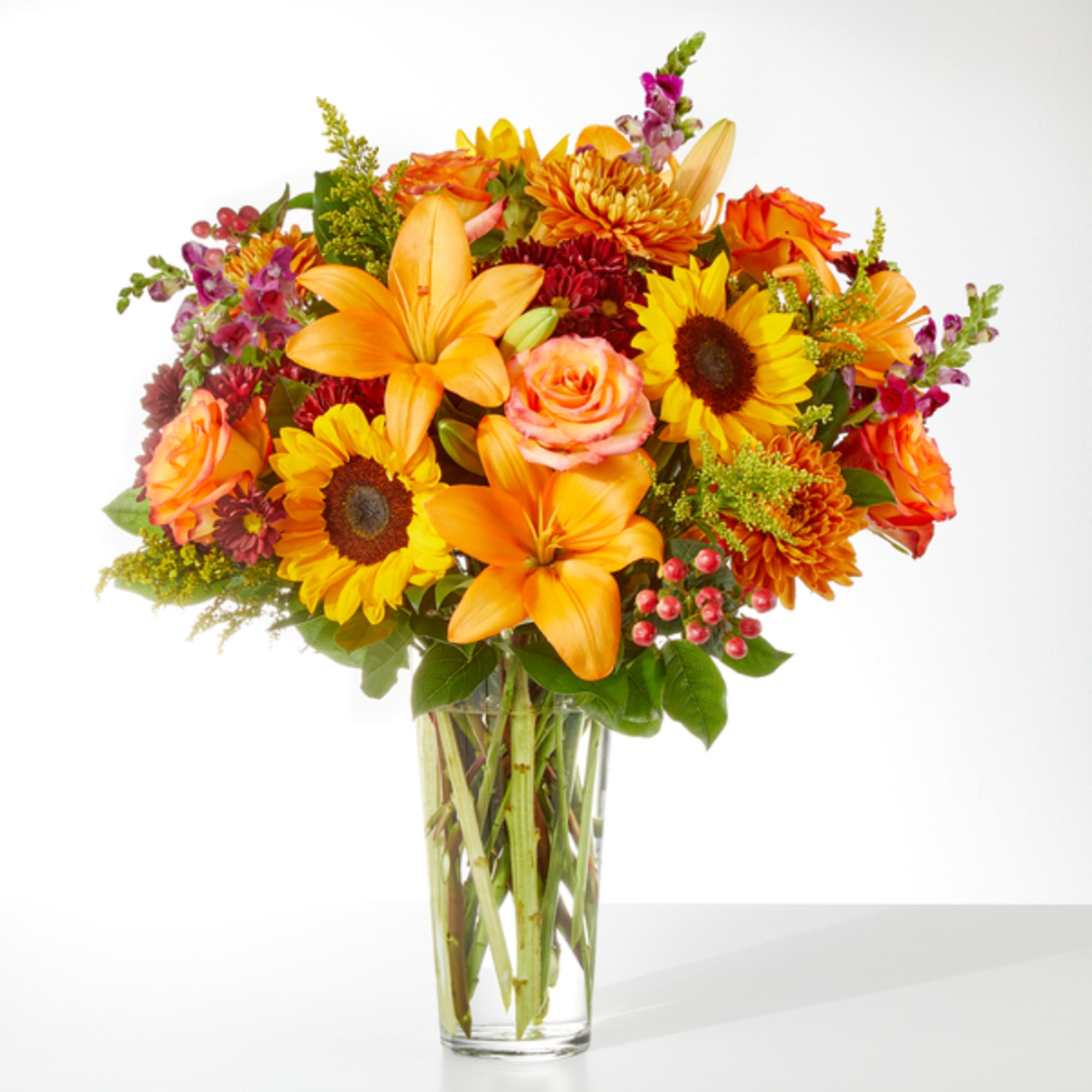 Bright mixed bouquet with sunflowers, lilies, roses, and chrysanthemums in a clear glass vase