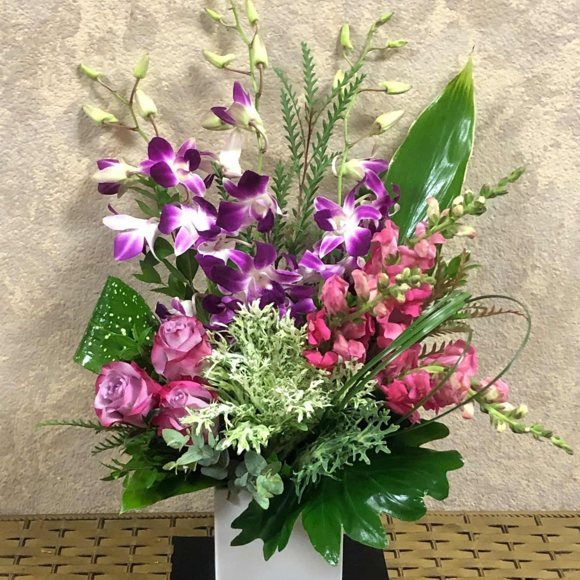 Purple orchids and pink flowers arranged in a white square vase