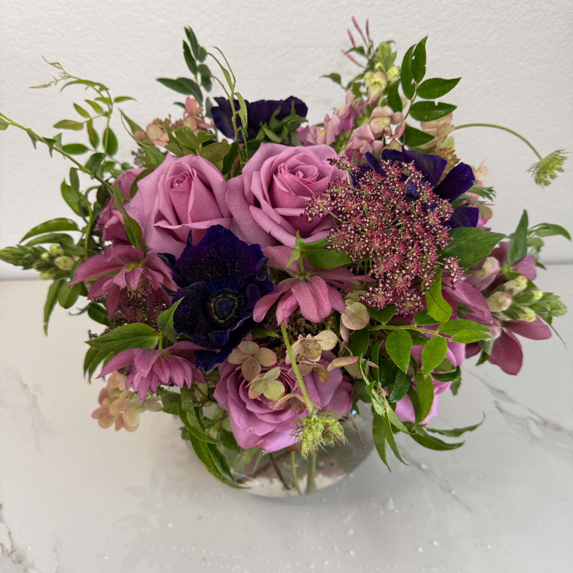 Lavender roses and purple flowers arranged in a clear glass vase