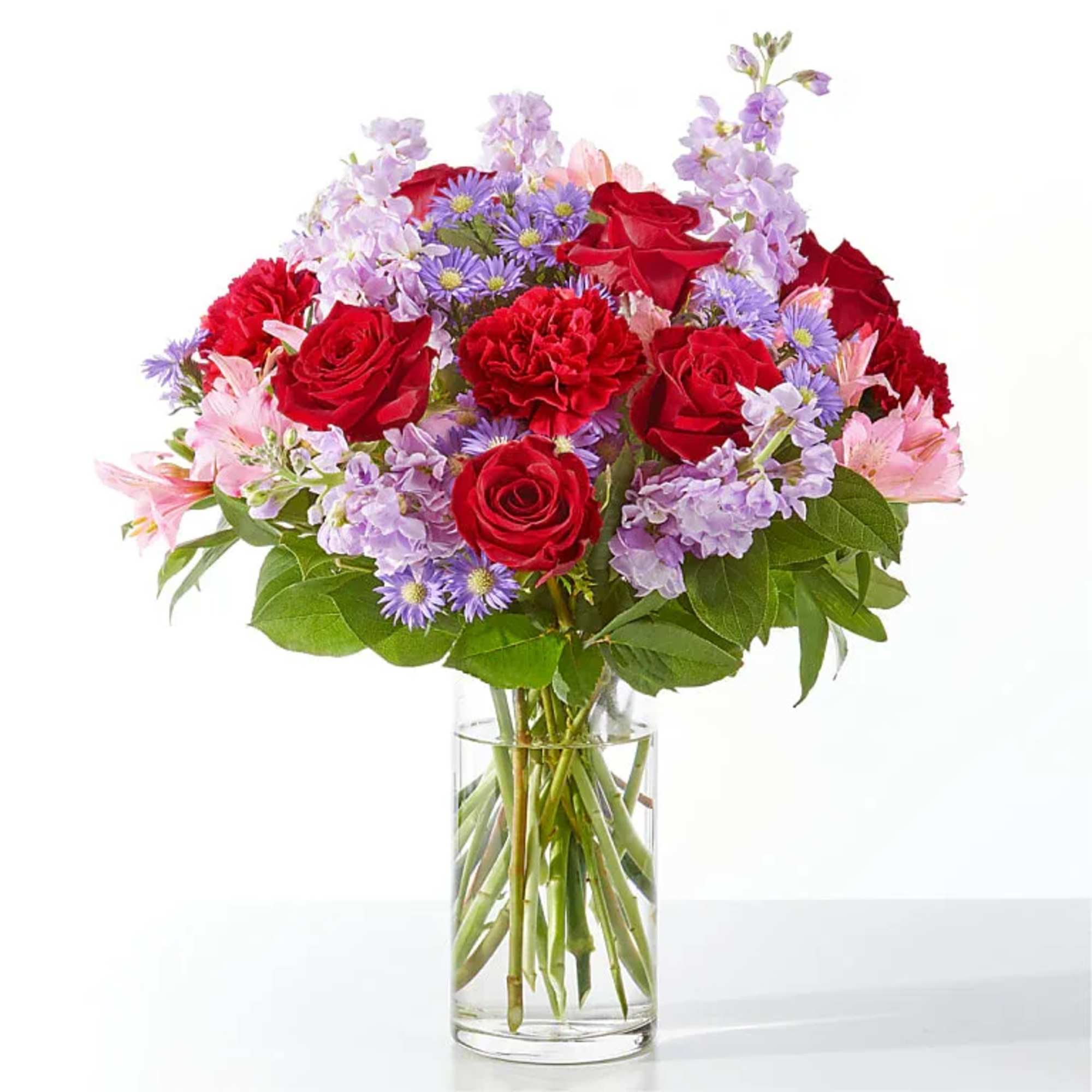 Bouquet of red roses, pink flowers, and purple blooms in a clear glass vase