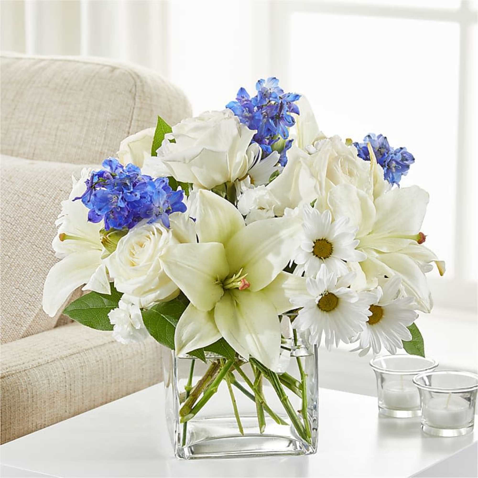 White lilies, roses, and daisies with blue flowers in a glass vase
