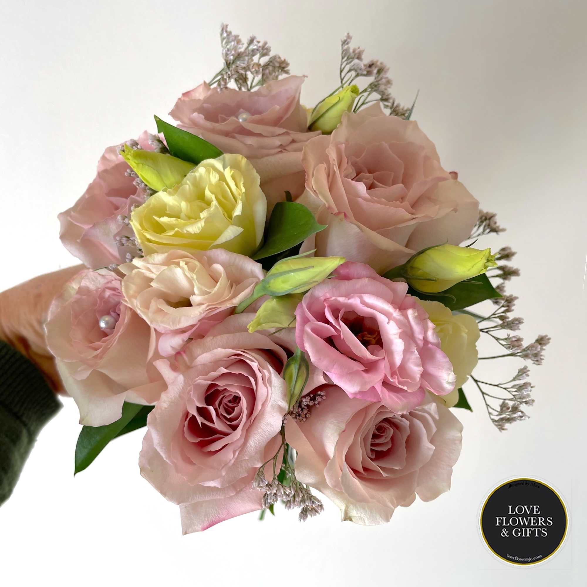 Handheld bouquet of pale pink roses and lisianthus with soft yellow buds.
